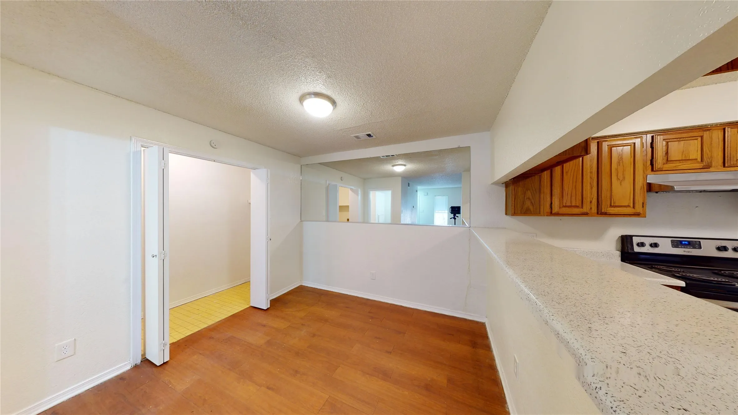 Kitchen with a textured ceiling, stainless steel range with electric stovetop, brown cabinetry, light wood-type flooring, and under cabinet range hood