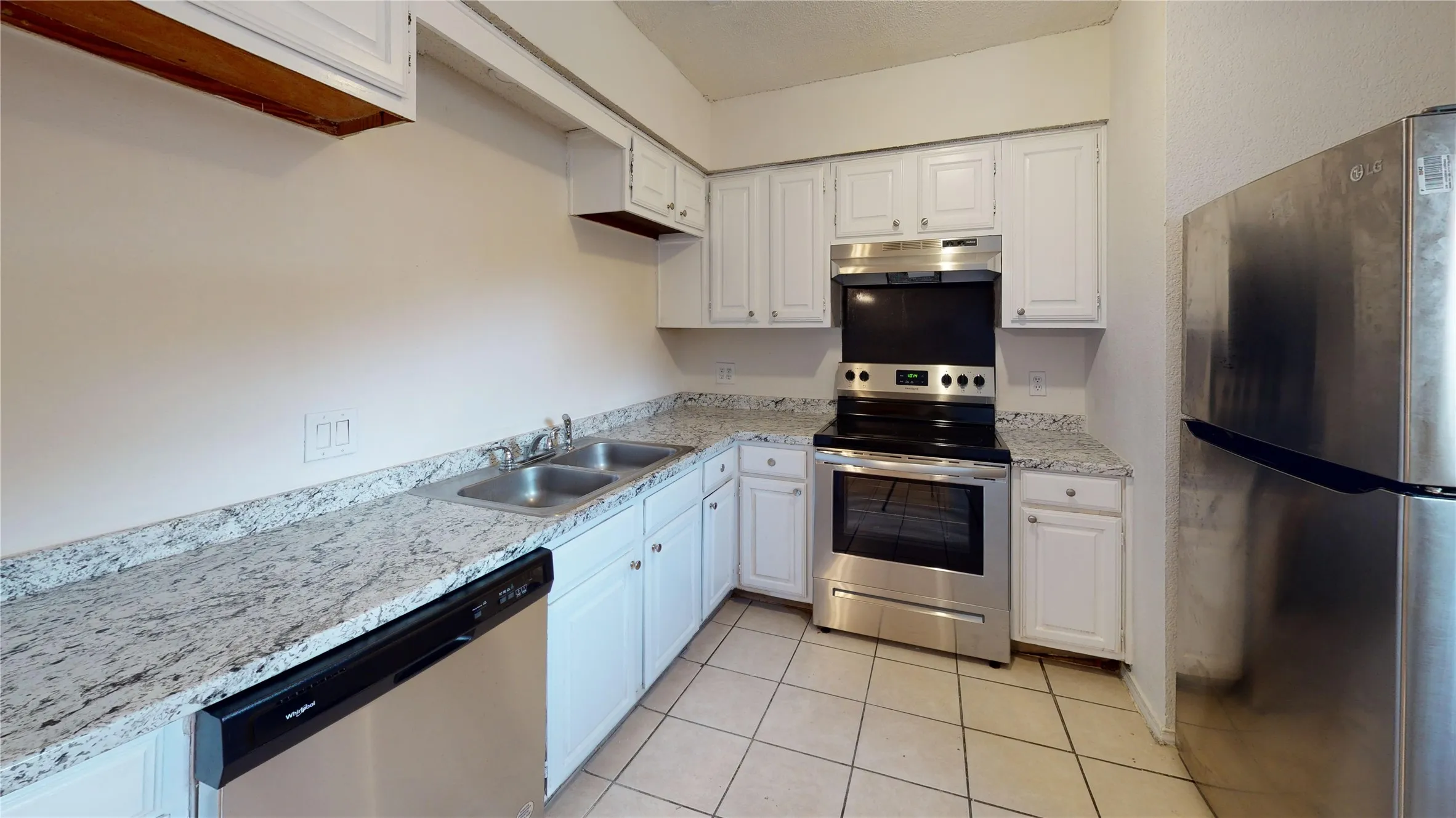Kitchen with appliances with stainless steel finishes, white cabinetry, under cabinet range hood, and light stone counters