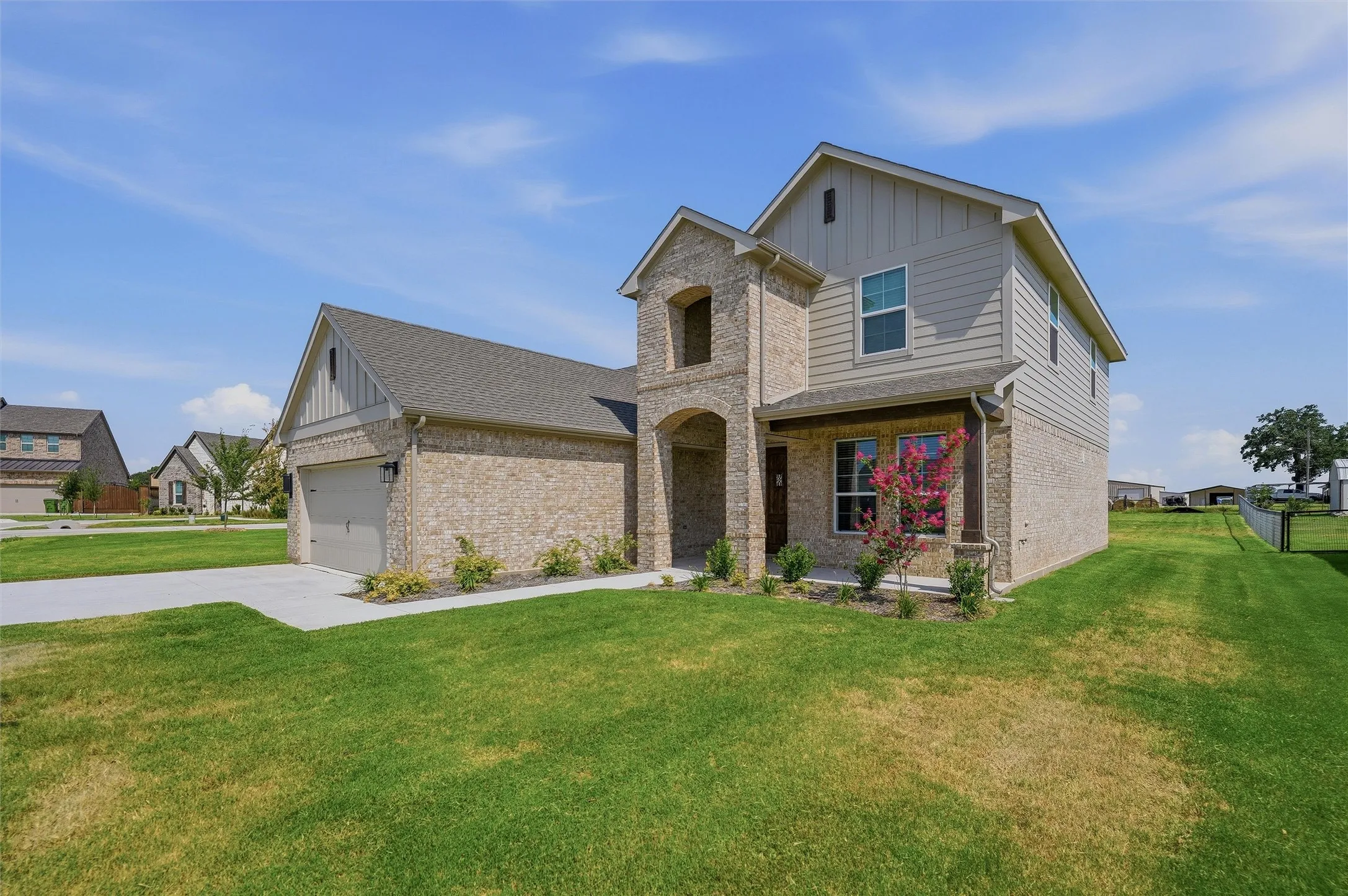 Two-story residence featuring a brick and siding exterior, an attached garage, a covered front porch, and a landscaped front yard with a concrete driveway