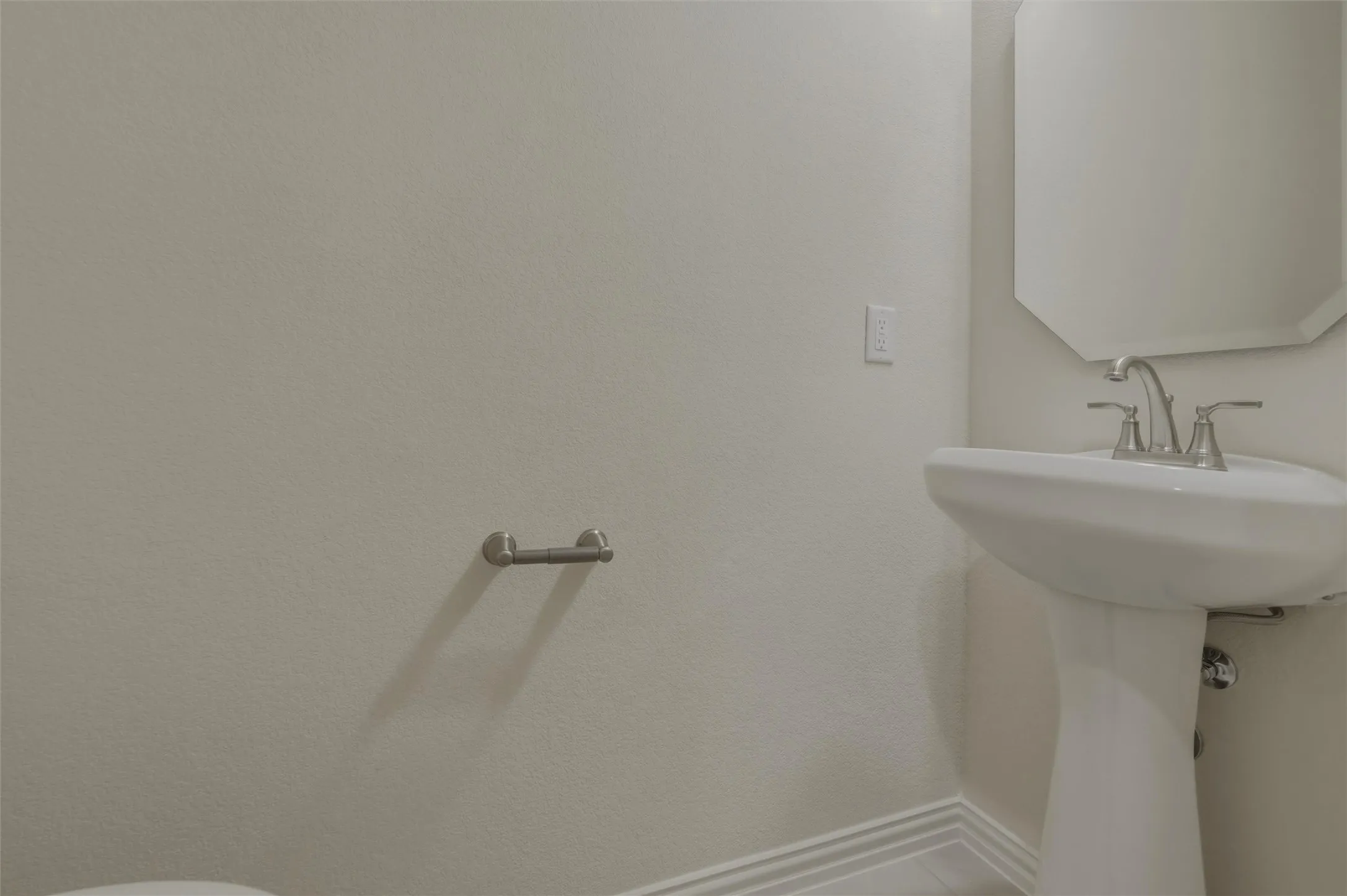 Pedestal sink with a polished chrome faucet, octagonal wall mirror, and neutral wall finish
