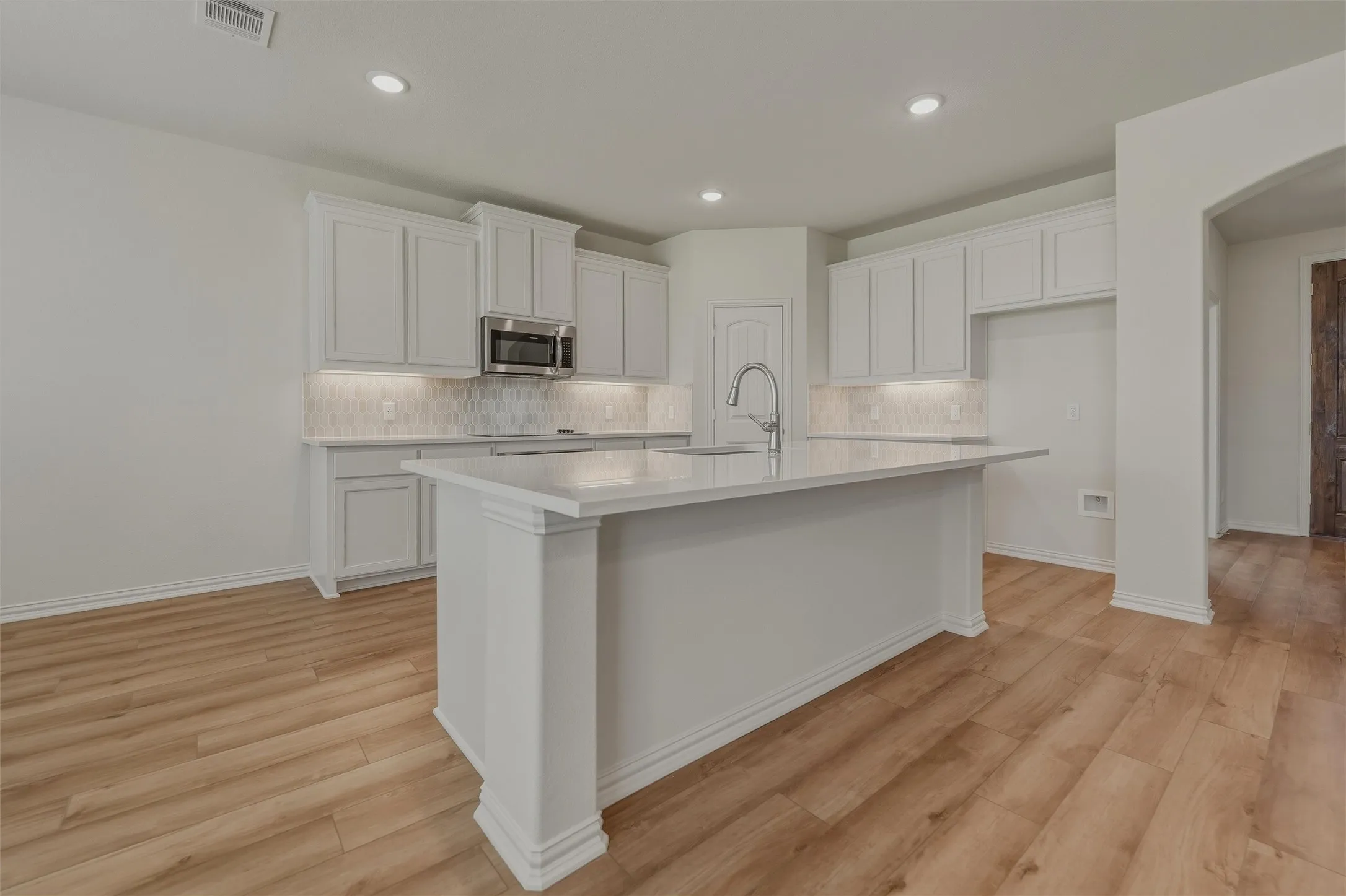 Kitchen featuring a central island, white cabinetry, undermount sink with gooseneck faucet, light-toned countertops, and wood-finish flooring