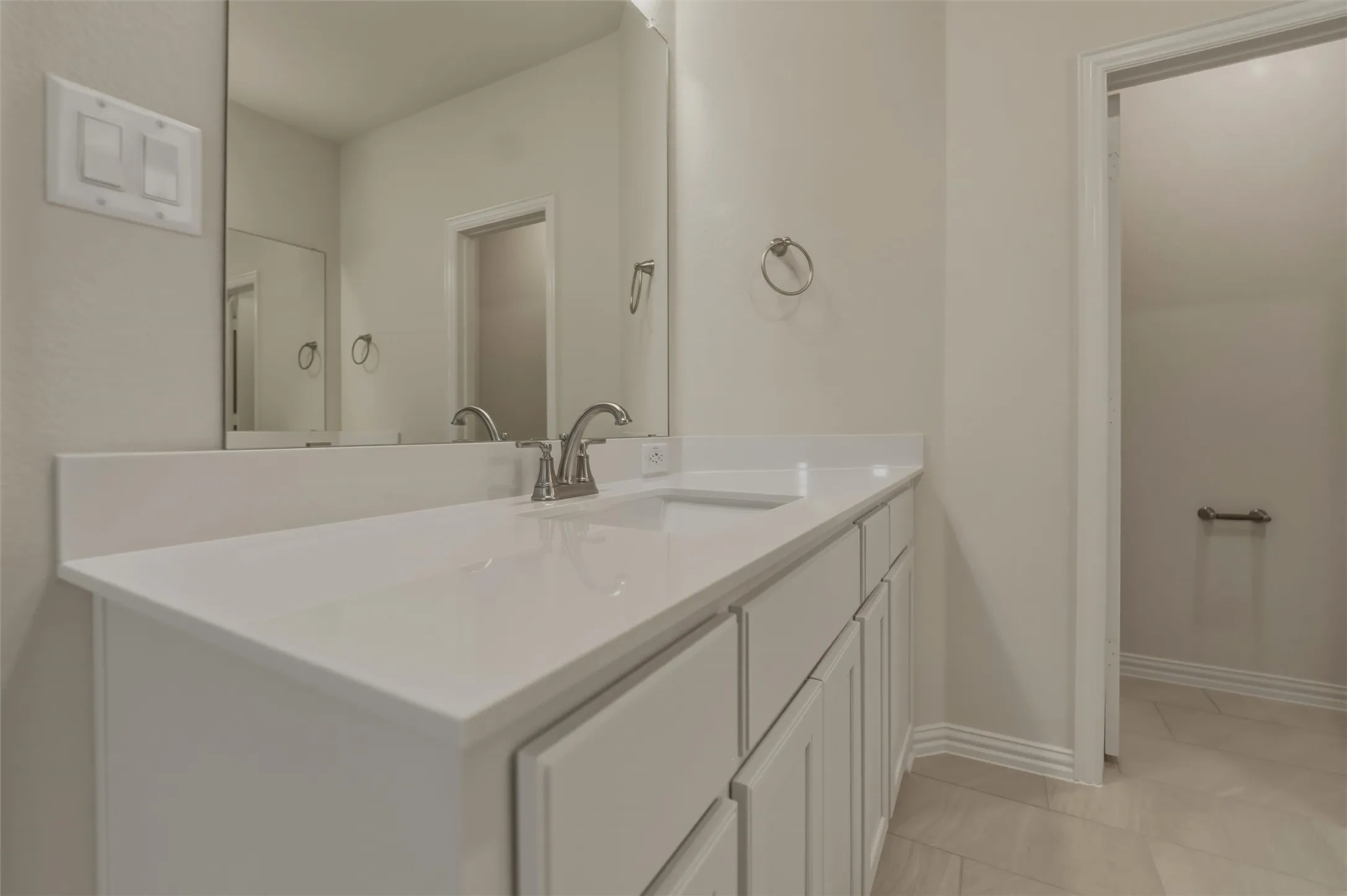 White vanity with integrated sink, polished chrome faucet, expansive vanity mirror, neutral wall paint, and tiled flooring