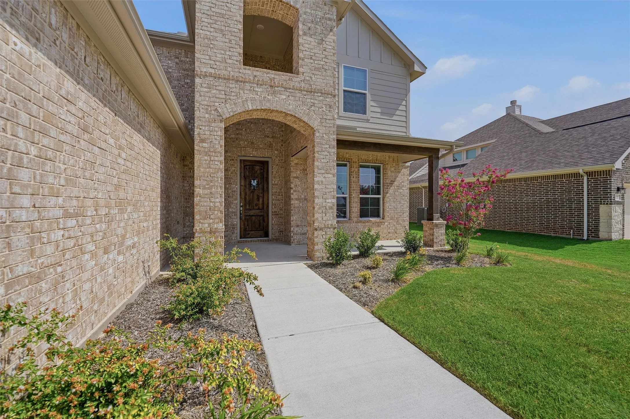 Brick and siding exterior with an arched entryway, covered porch, and concrete walkway