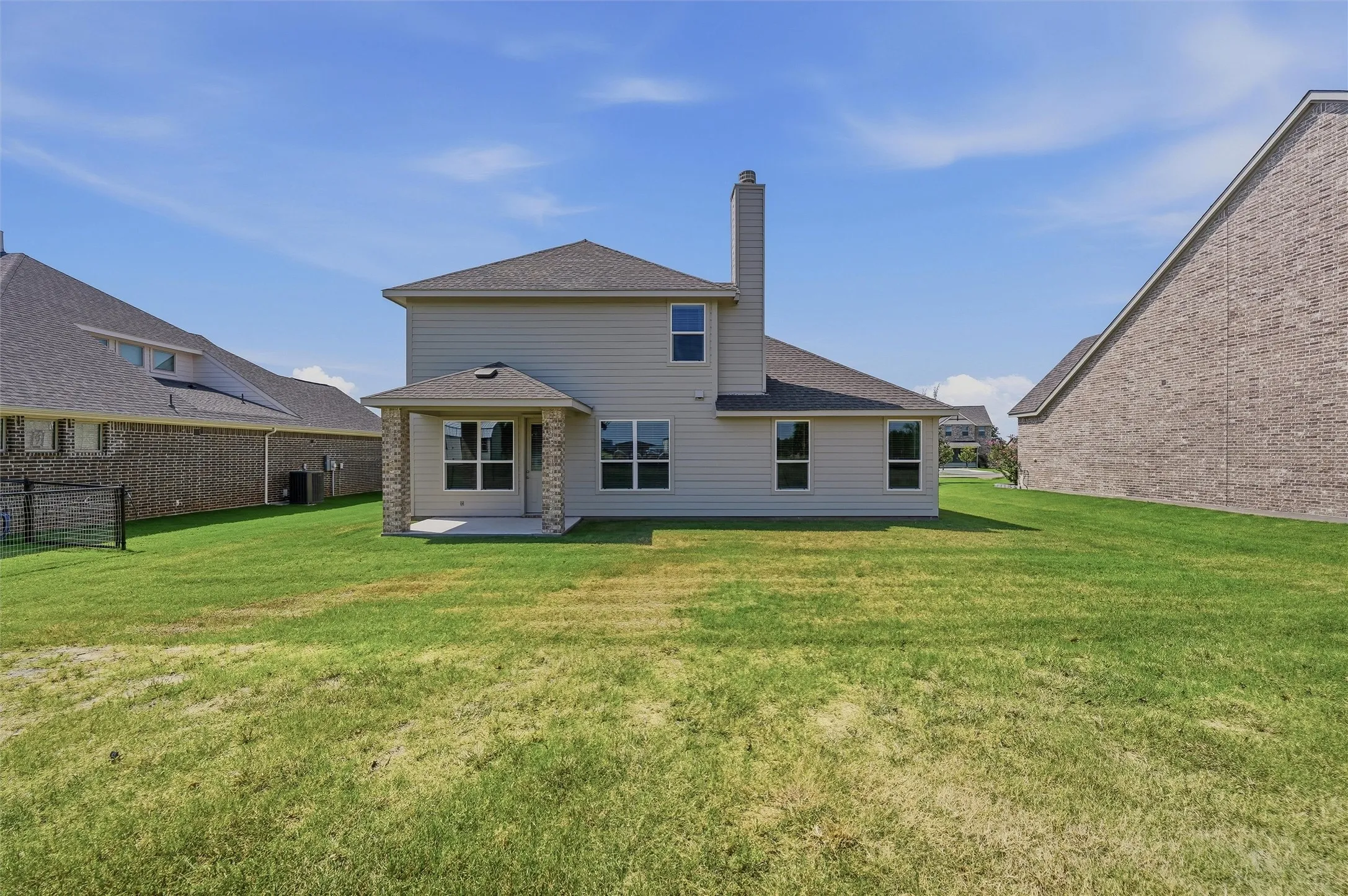 Spacious two-story home with brick and siding exterior, featuring a covered rear patio, chimney, and expansive manicured lawn with mature landscaping in a residential setting
