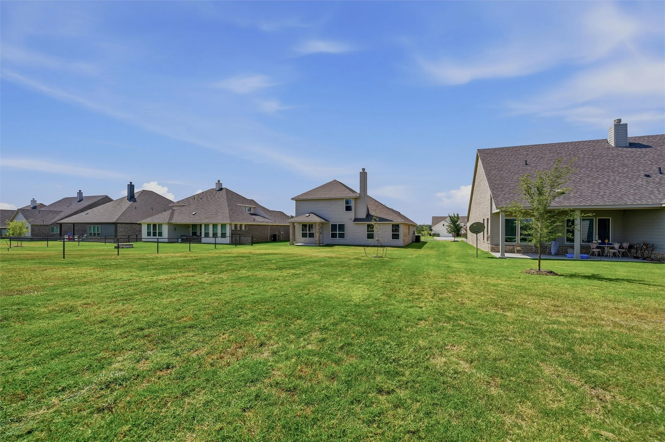 Expansive grass lawn with a covered patio and a partially brick exterior