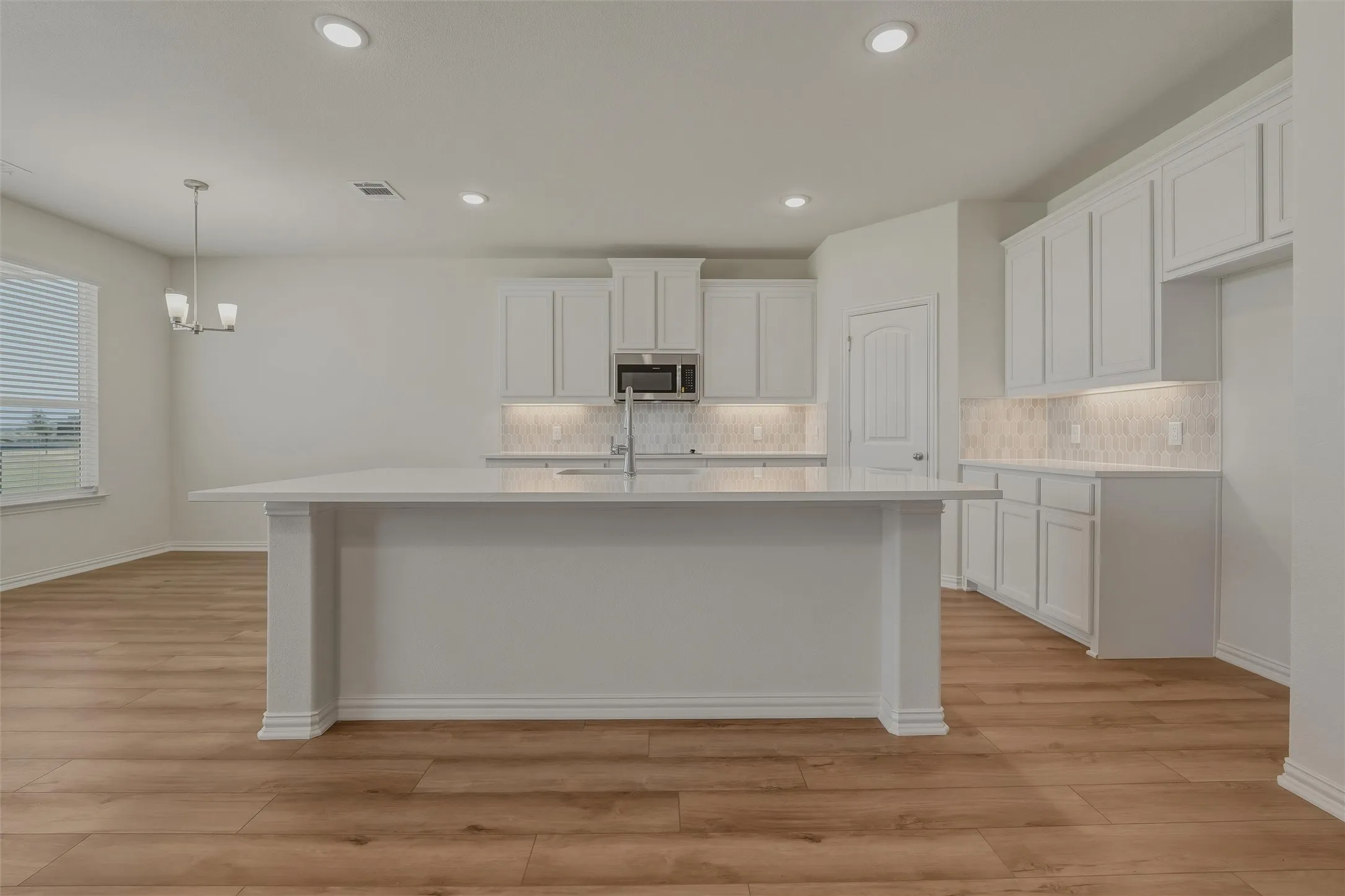 Expansive kitchen island with a light-toned countertop, wood-finish flooring, white cabinetry, and recessed lighting
