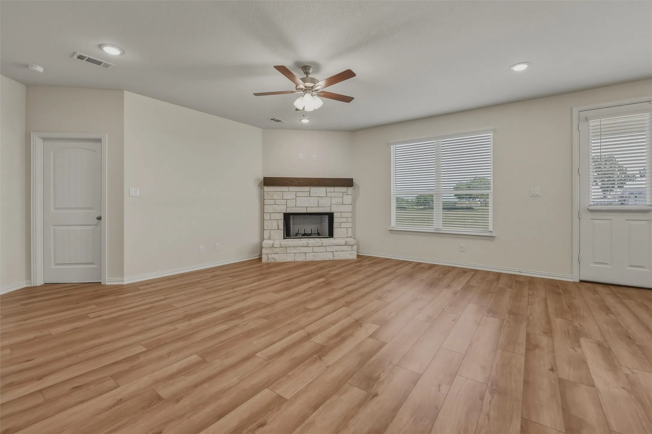 Wood-finish flooring, corner fireplace with stone surround and wood mantel, ceiling fan with integrated lighting, recessed lighting, and white window blinds
