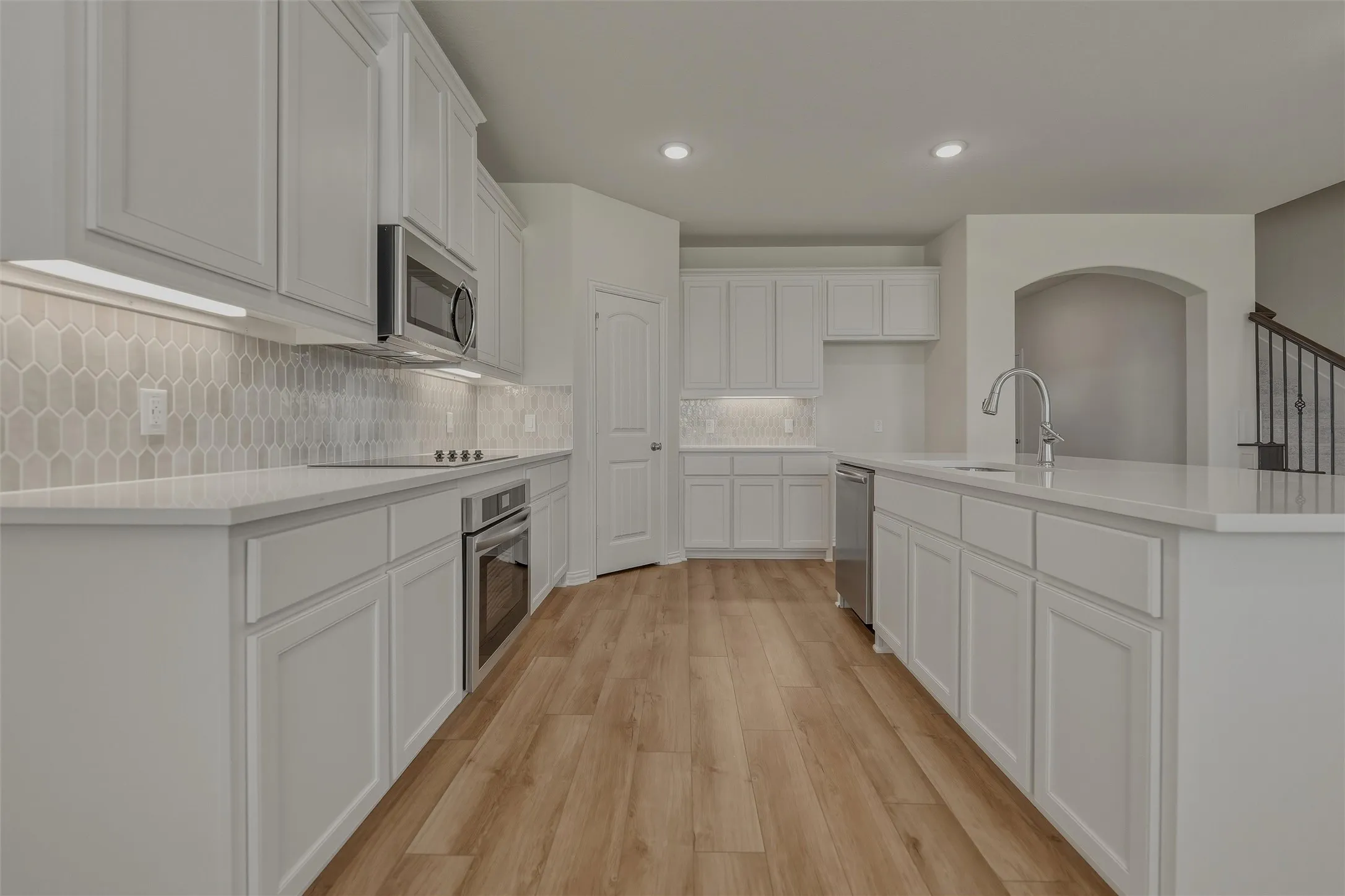 Kitchen featuring light wood-finish flooring, white cabinetry, integrated stainless steel appliances, a center island with a sink, and a tile backsplash