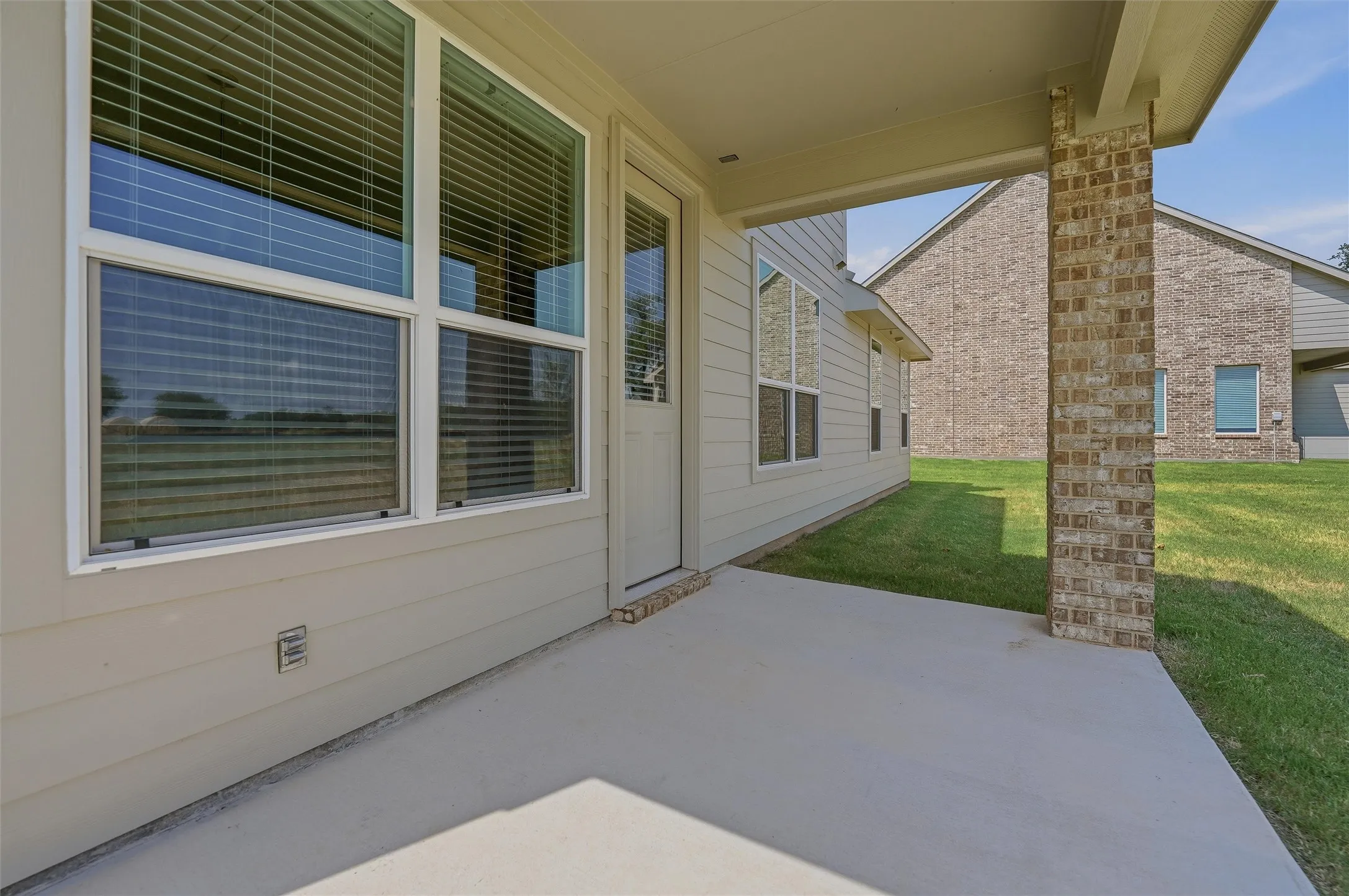 Covered patio featuring a concrete floor, large multi-pane sliding glass doors with integrated blinds, and brick column support