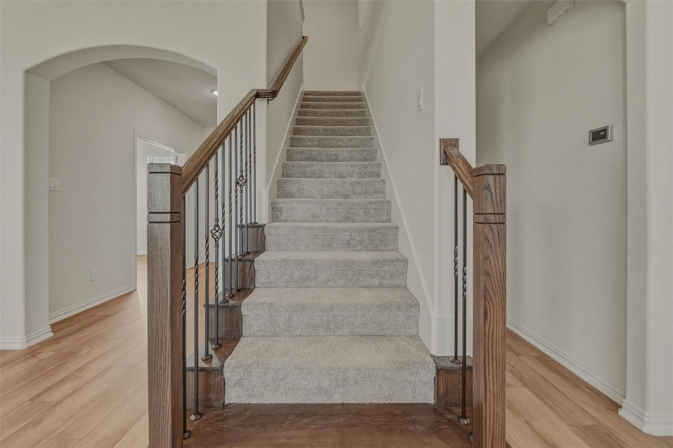 Staircase with wood-finish handrails, decorative wrought iron balusters, and light gray carpeted treads