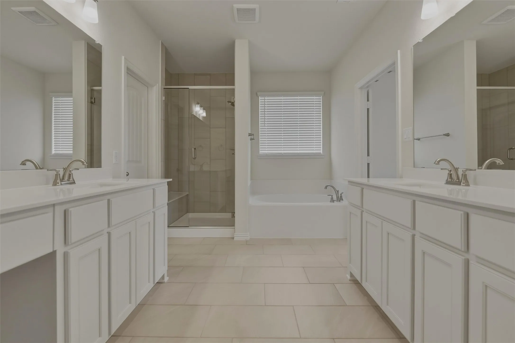 Dual vanities with white cabinetry, a glass-enclosed shower, built-in bathtub, and tile flooring