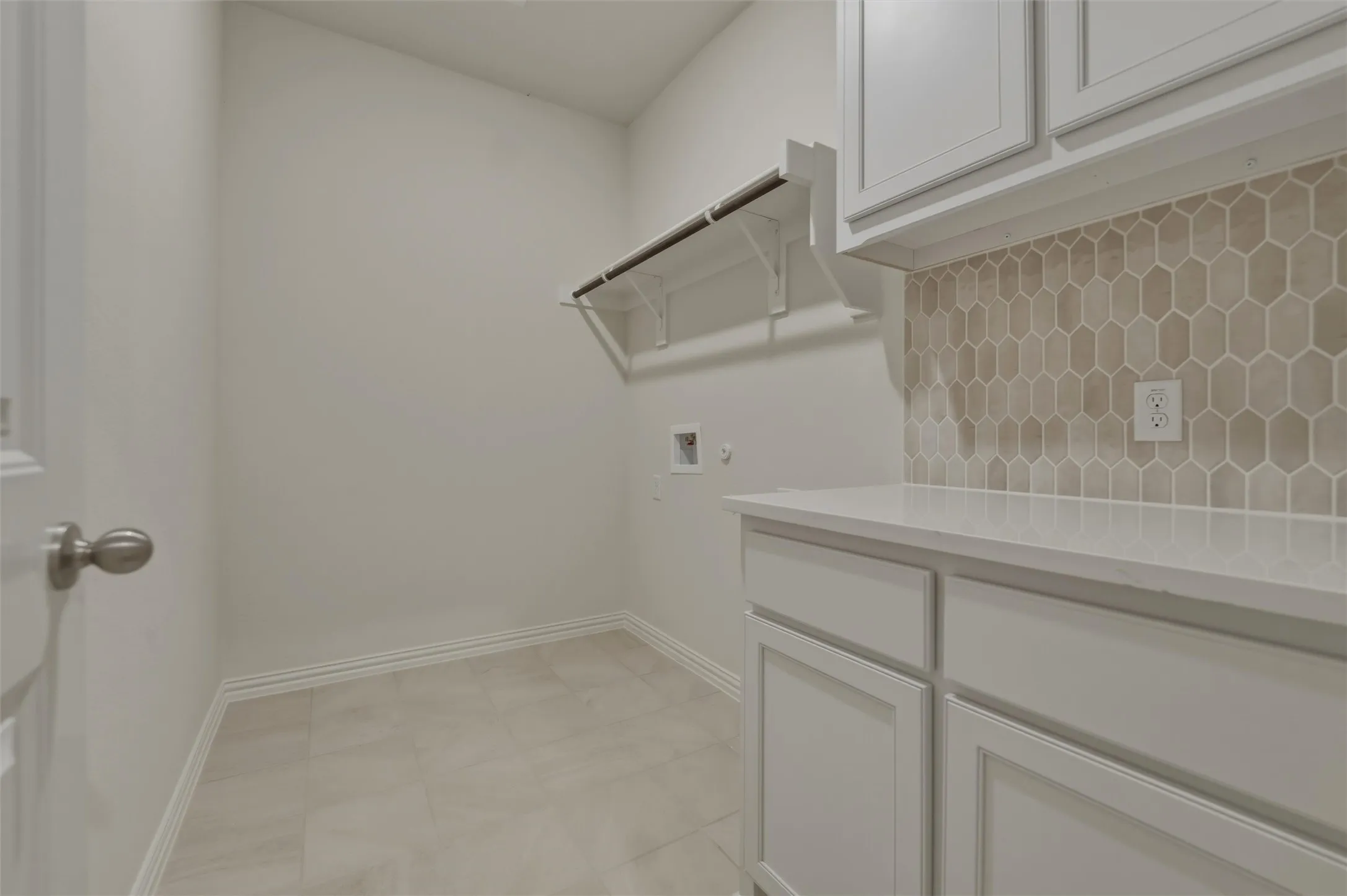 Neutral-toned tile flooring, built-in shelving, white cabinetry, integrated countertop, and geometric tile backsplash
