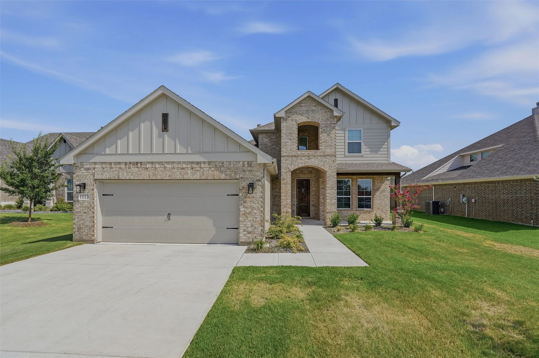 Brick and siding exterior with a two-car garage, concrete driveway, and front walkway