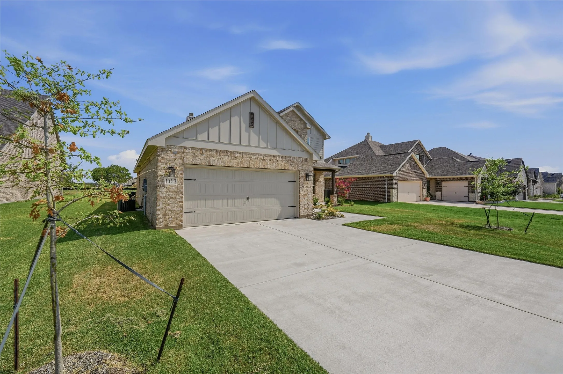 Brick exterior with board and batten siding, attached garage, and concrete driveway