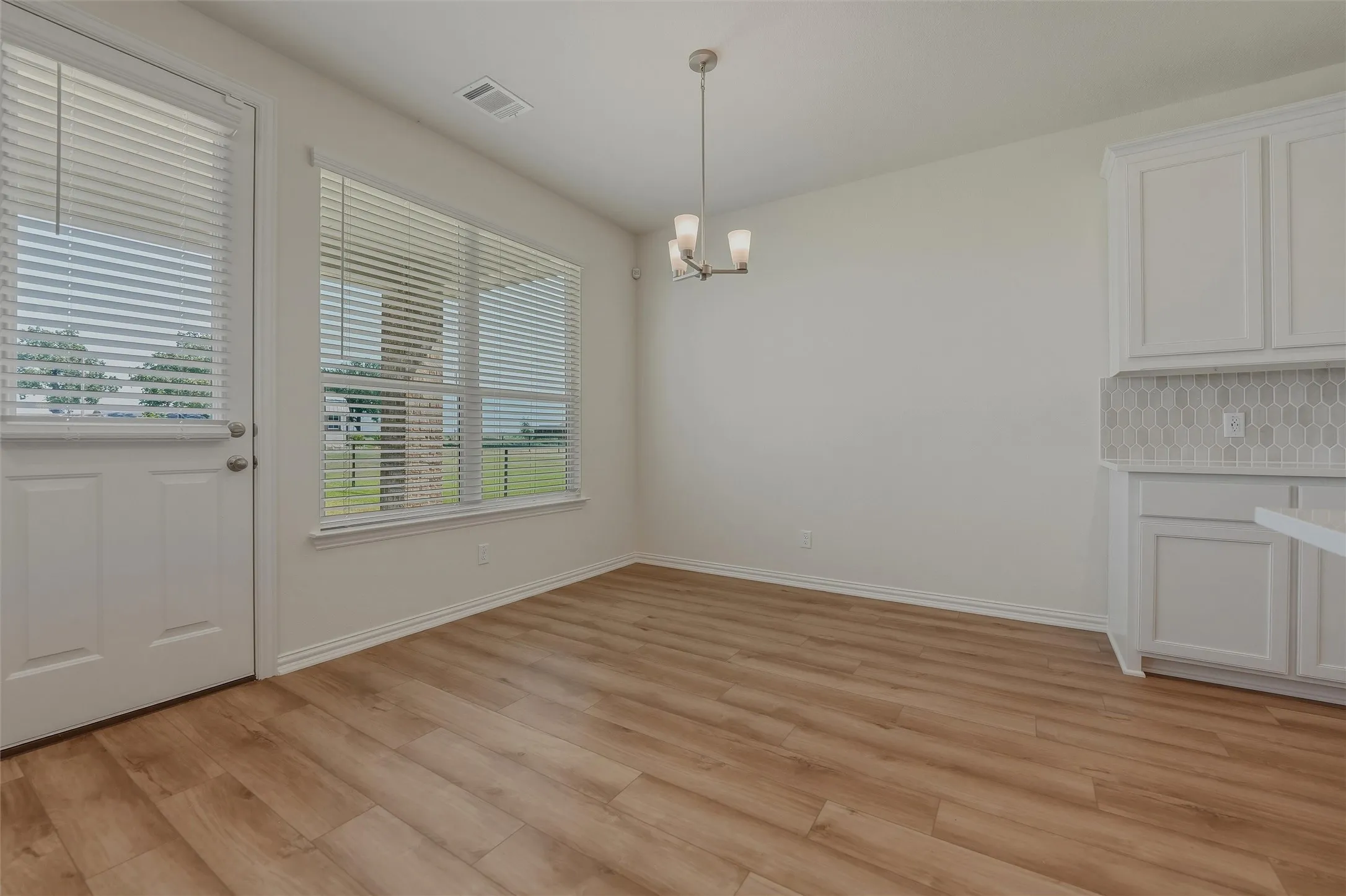 Wood-finish flooring, white cabinetry, decorative tile backsplash, and a modern chandelier