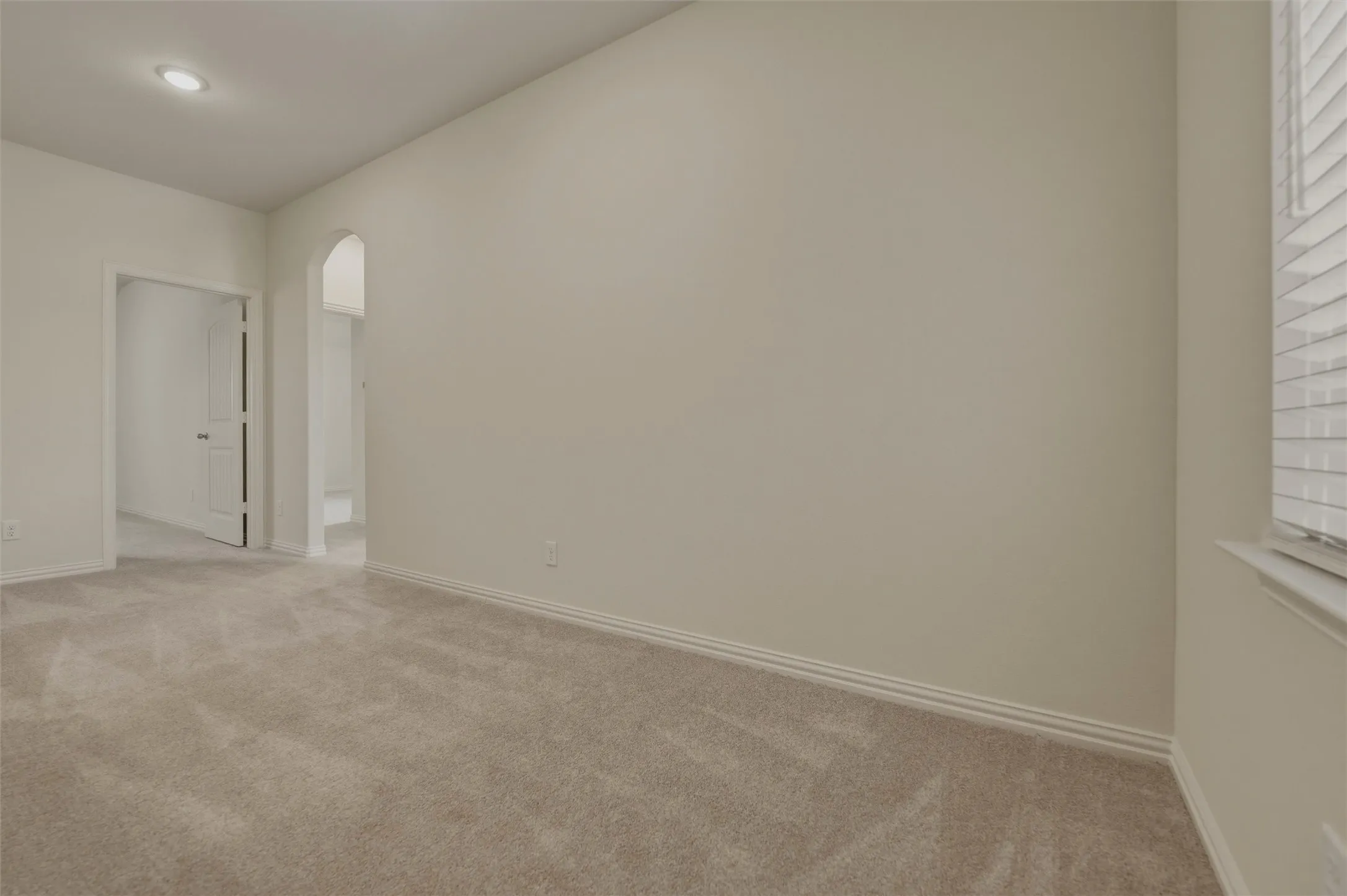Neutral tone wall, carpeted flooring, recessed ceiling light, arched doorway, and window with horizontal blinds