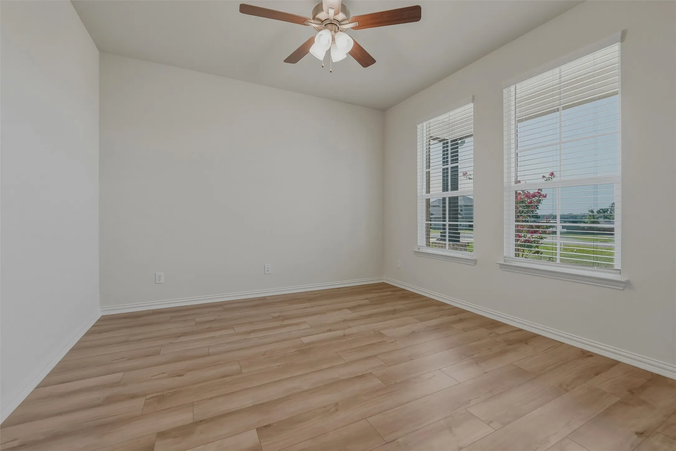 Wood-finish flooring, two large windows with blinds, and a ceiling fan with integrated lighting