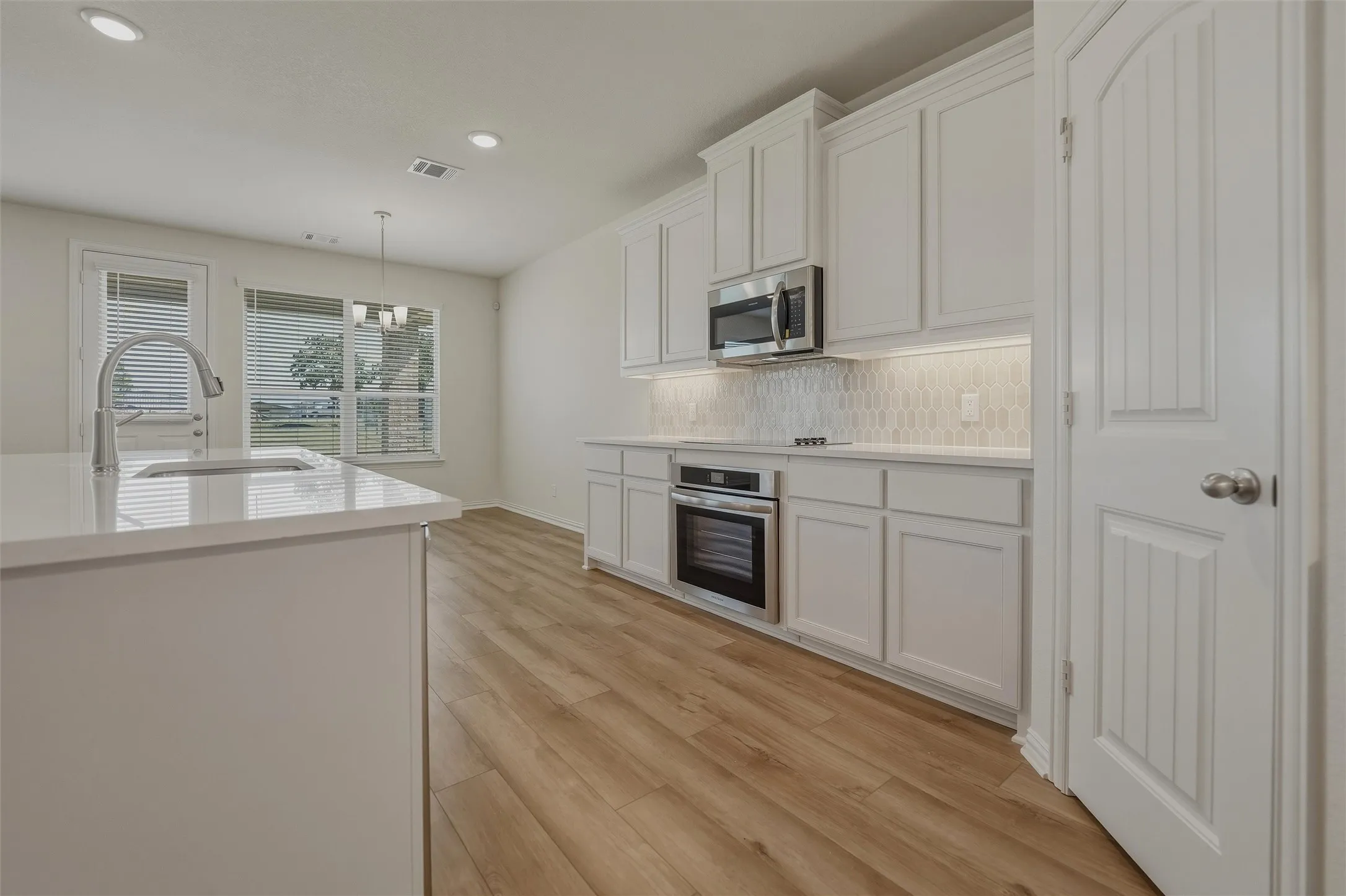 Modern kitchen featuring white cabinetry with raised-panel doors, stainless steel built-in appliances including a microwave and wall oven, quartz countertops, subway tile backsplash, and a large island with waterfall edge