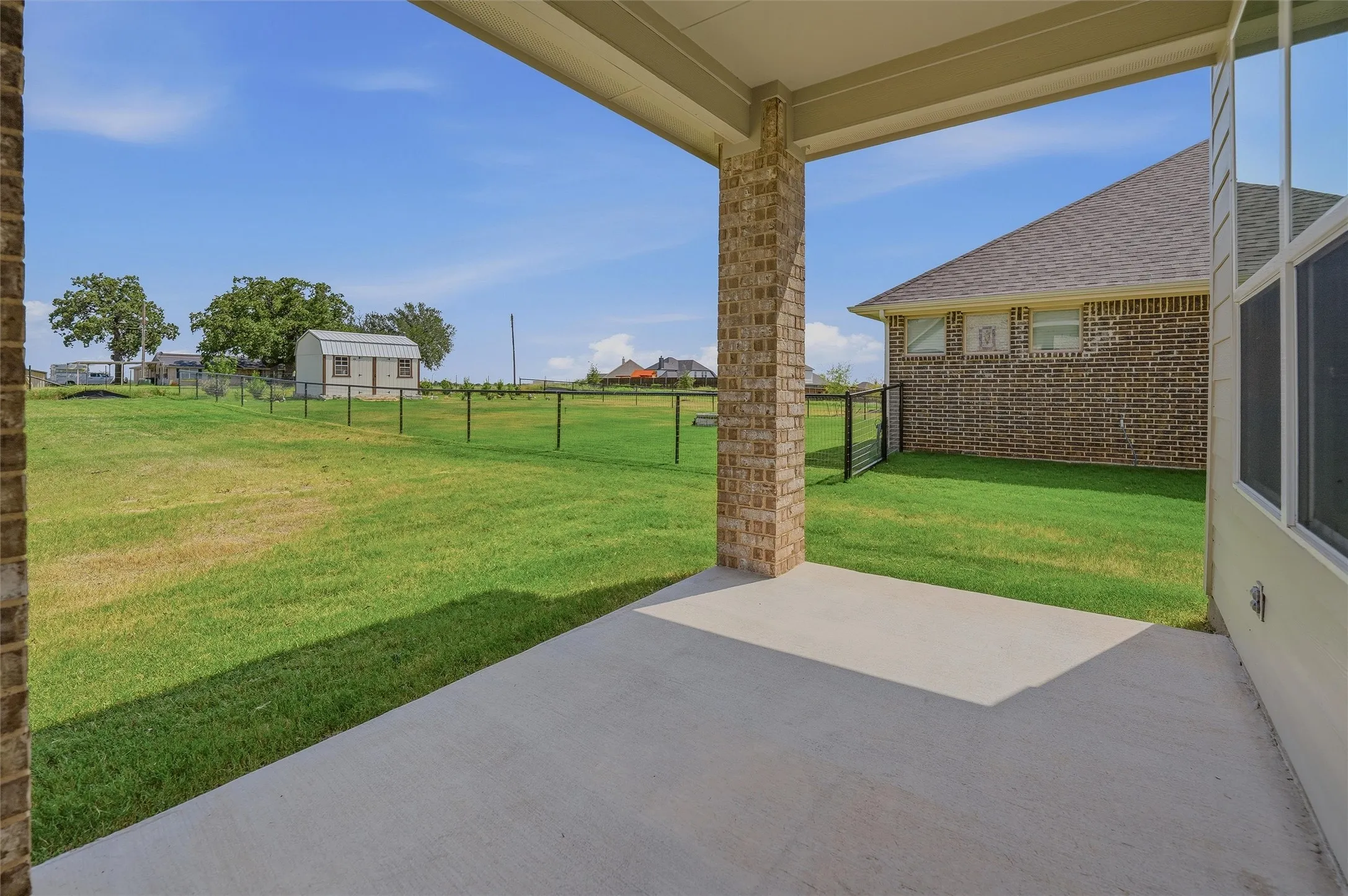 Covered concrete patio with a brick pillar, overlooking a fenced grassy yard