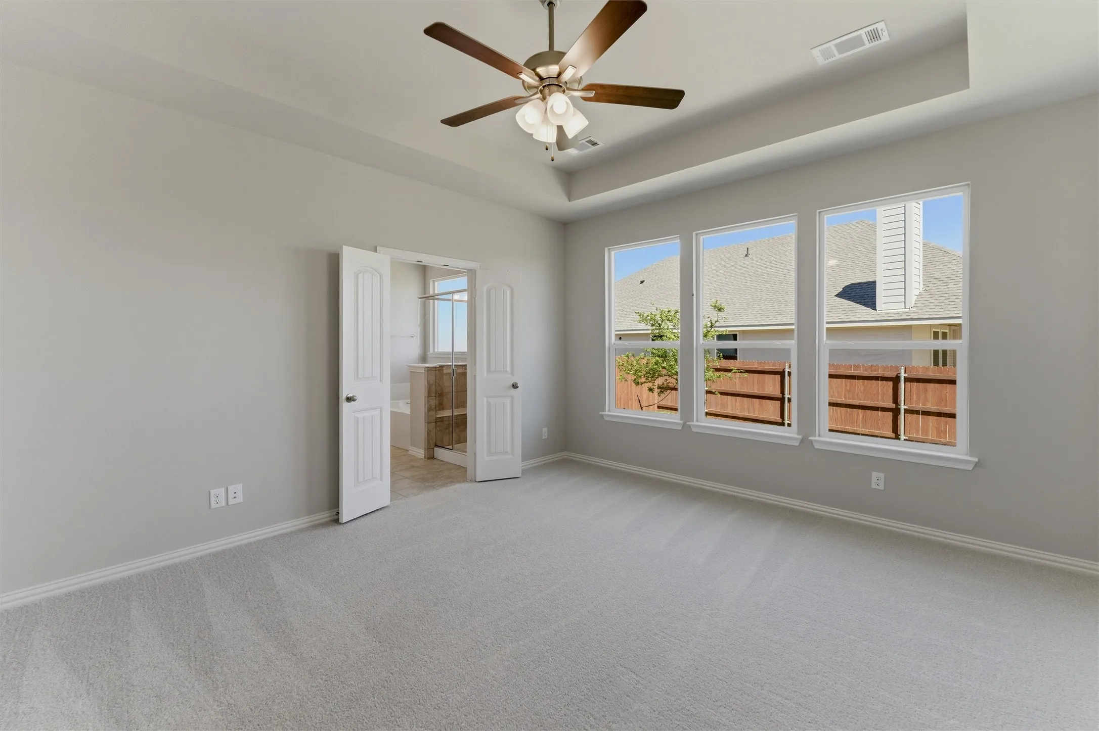 Empty room with light carpet, a raised ceiling, and ceiling fan