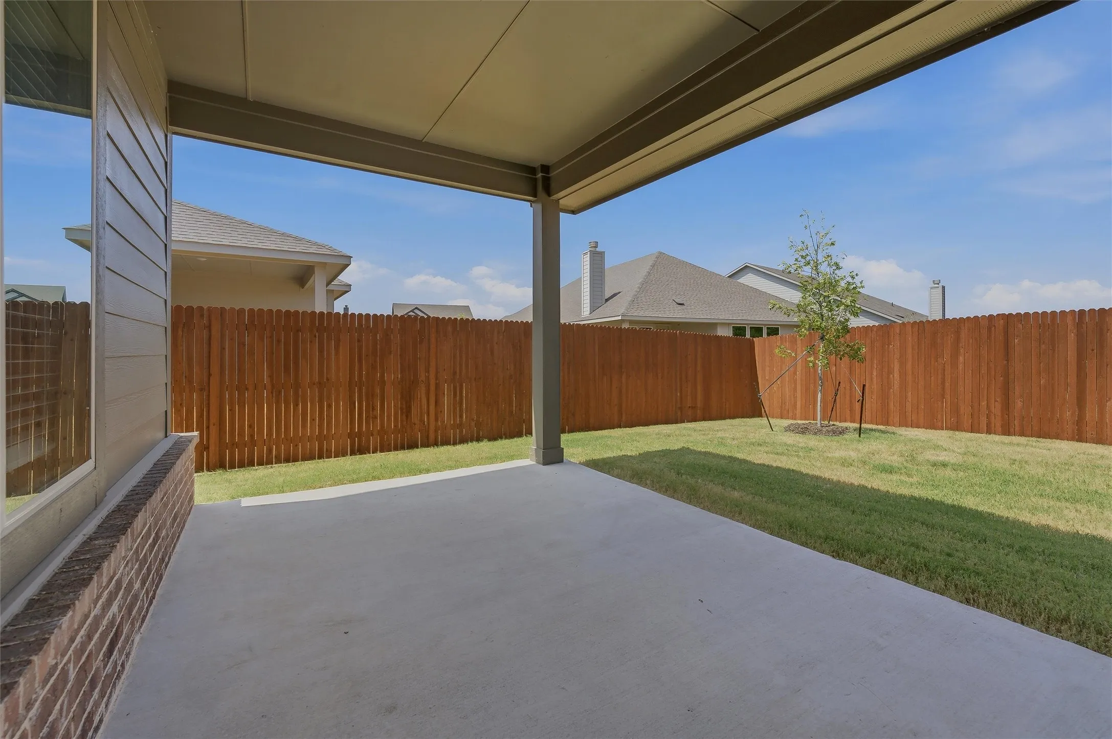 Covered patio with concrete flooring, bordered by a privacy fence and a manicured lawn