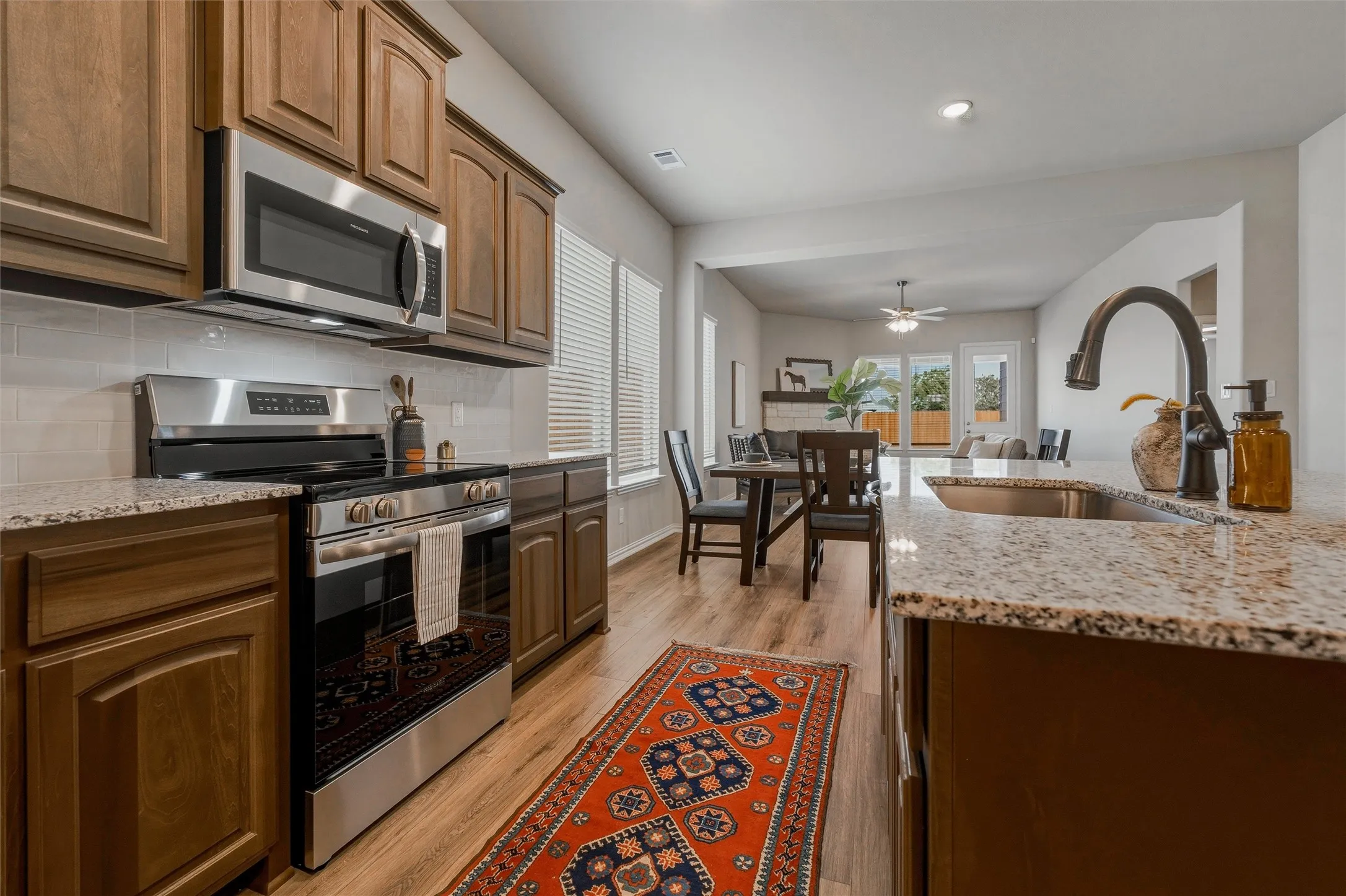 Kitchen featuring wood-finish cabinetry, stainless steel appliances, speckled stone countertops, and a subway tile backsplash
