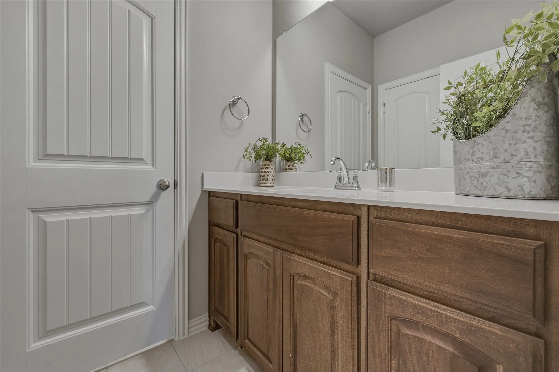 White countertop, wood-finish cabinetry, ceramic tile flooring, and a large wall mirror