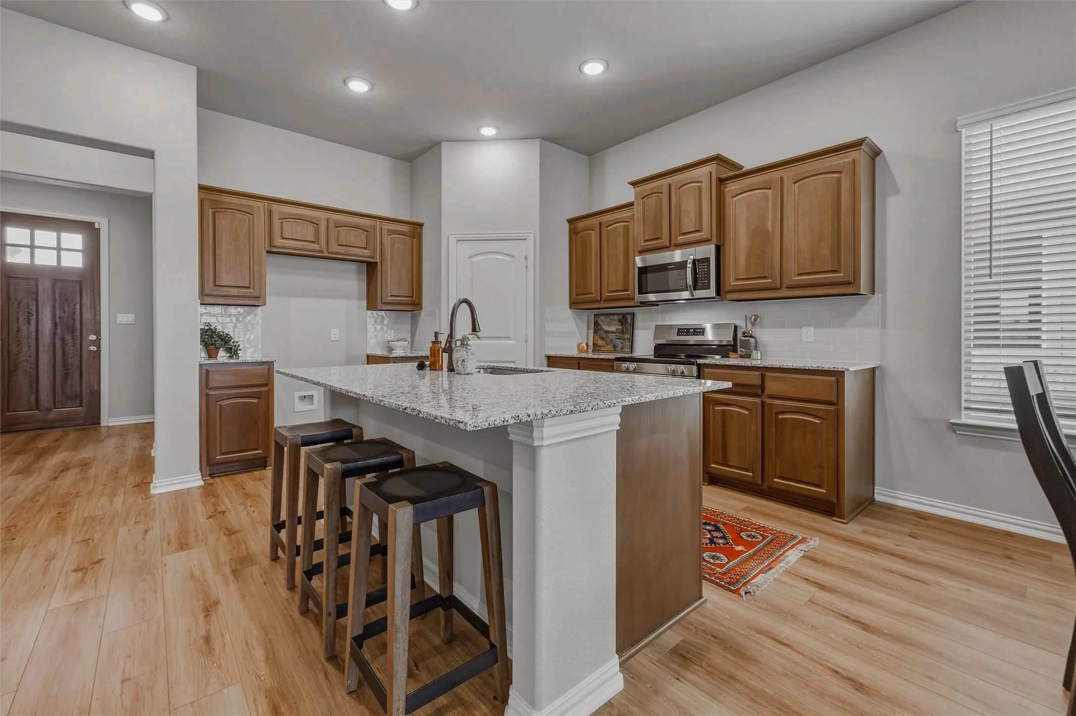 Kitchen featuring wood-finish flooring, recessed lighting, a central island with a sink, granite countertops, and wood cabinetry