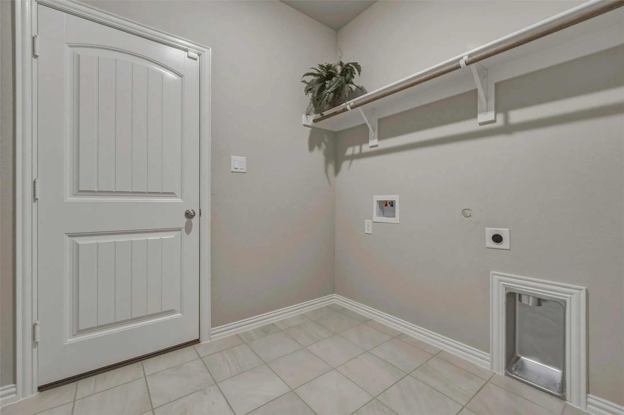 Utility area featuring tile flooring, a paneled door, built-in shelving, and a hanging rod