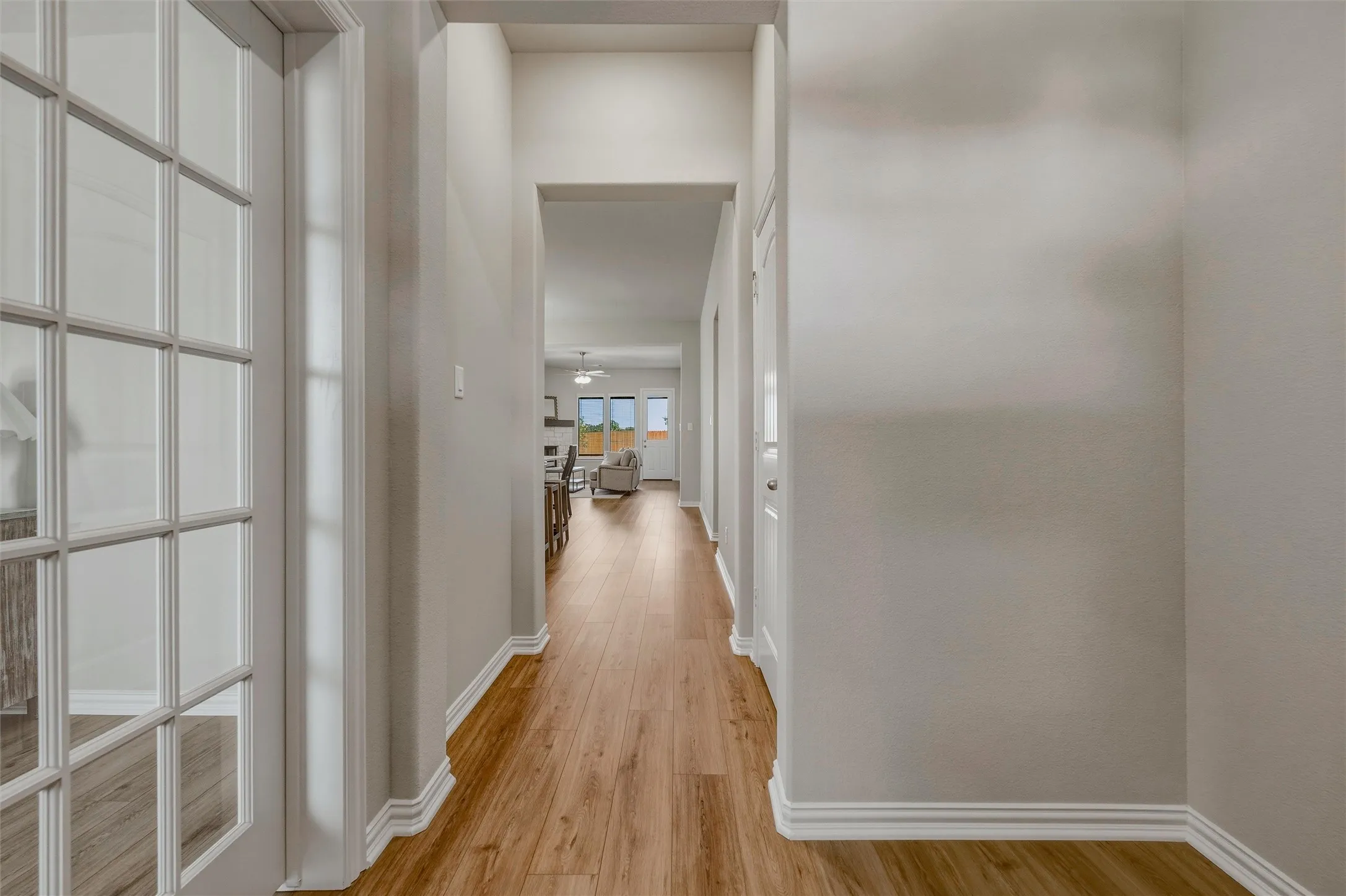 Hallway featuring wood-finish flooring, light neutral wall paint, white trim, and a French door with clear glass panels