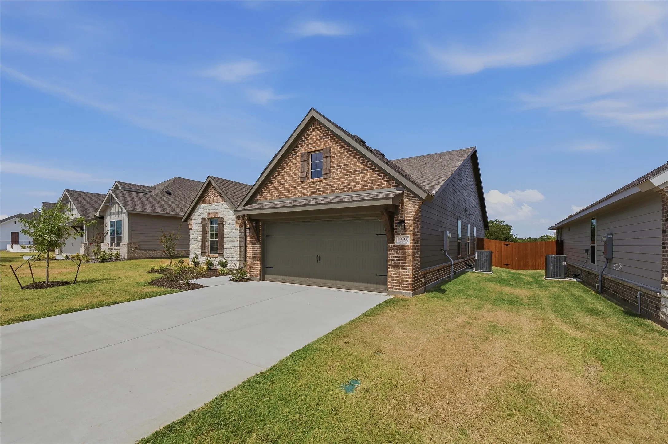 Brick and stone façade with an attached garage, concrete driveway, and side yard