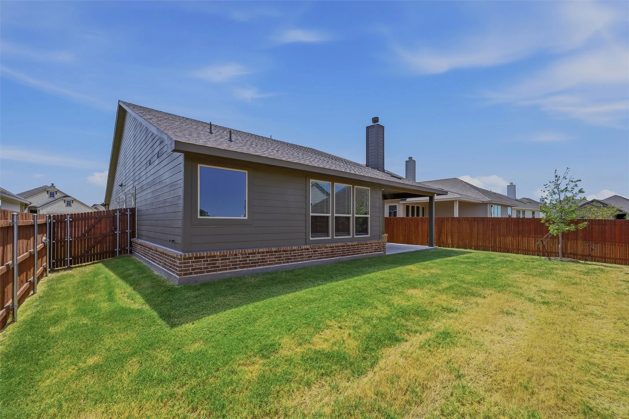 Expansive backyard featuring a manicured lawn, wood fencing, and a covered patio