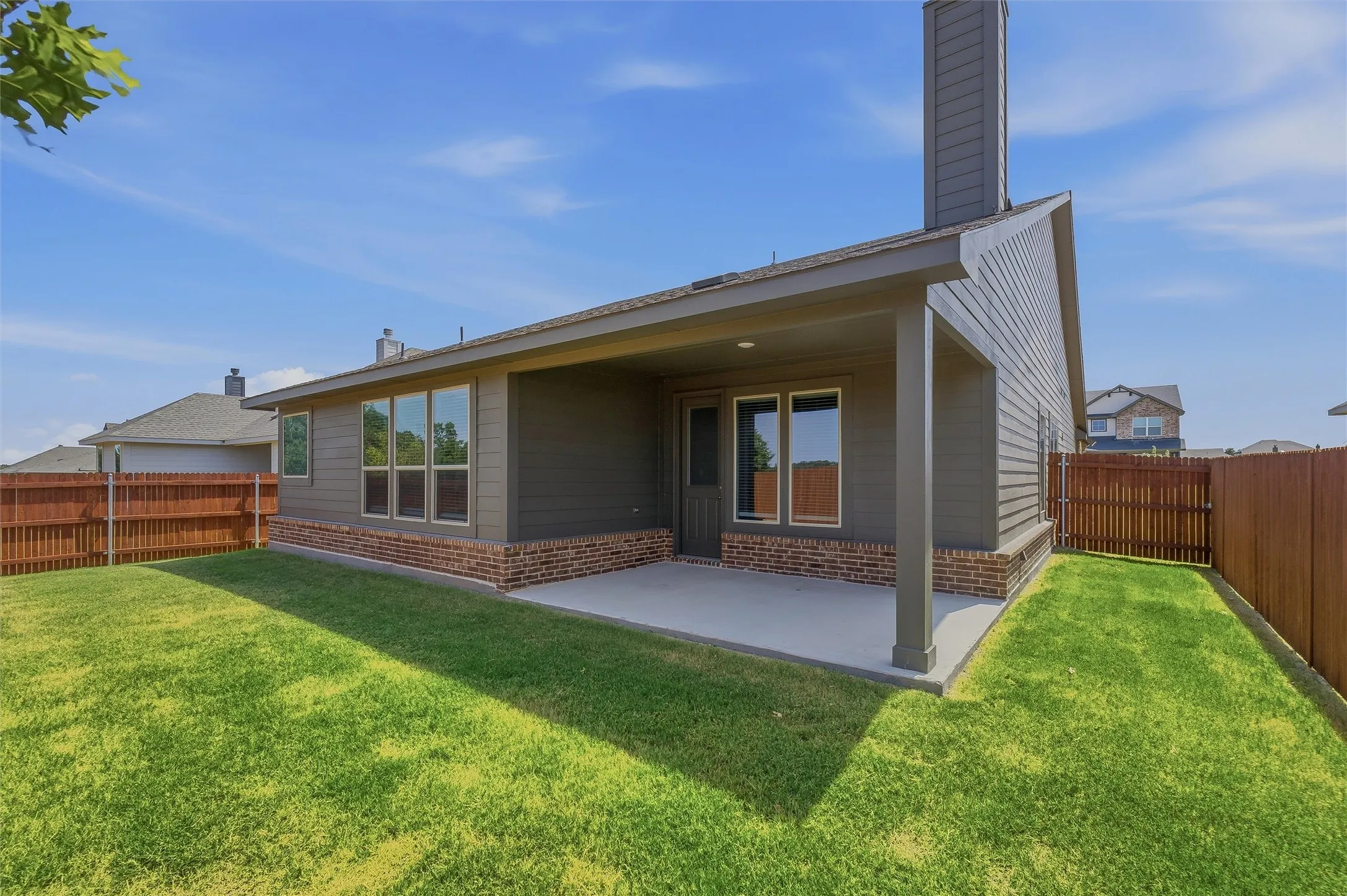 Expansive backyard featuring a manicured lawn, full privacy fencing, and a covered patio with brick veneer accents