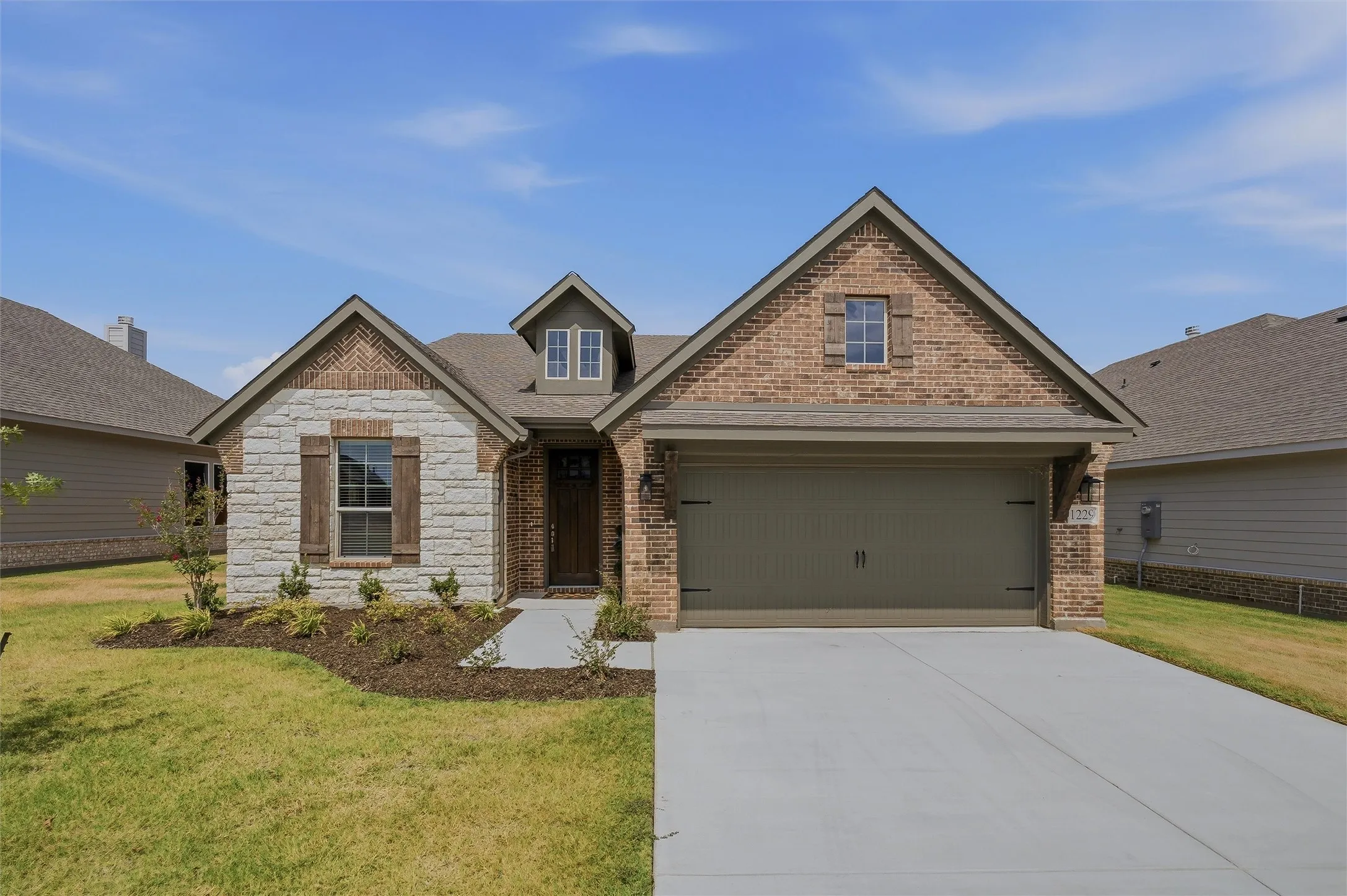 Brick and stone facade with gabled roof lines, attached two-car garage, concrete driveway, and established front landscaping