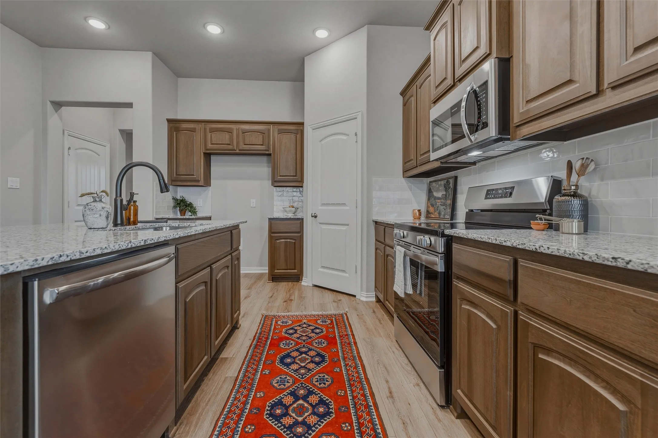 Kitchen featuring wood-finish cabinetry, stainless steel appliances, speckled stone countertops, and a white subway tile backsplash