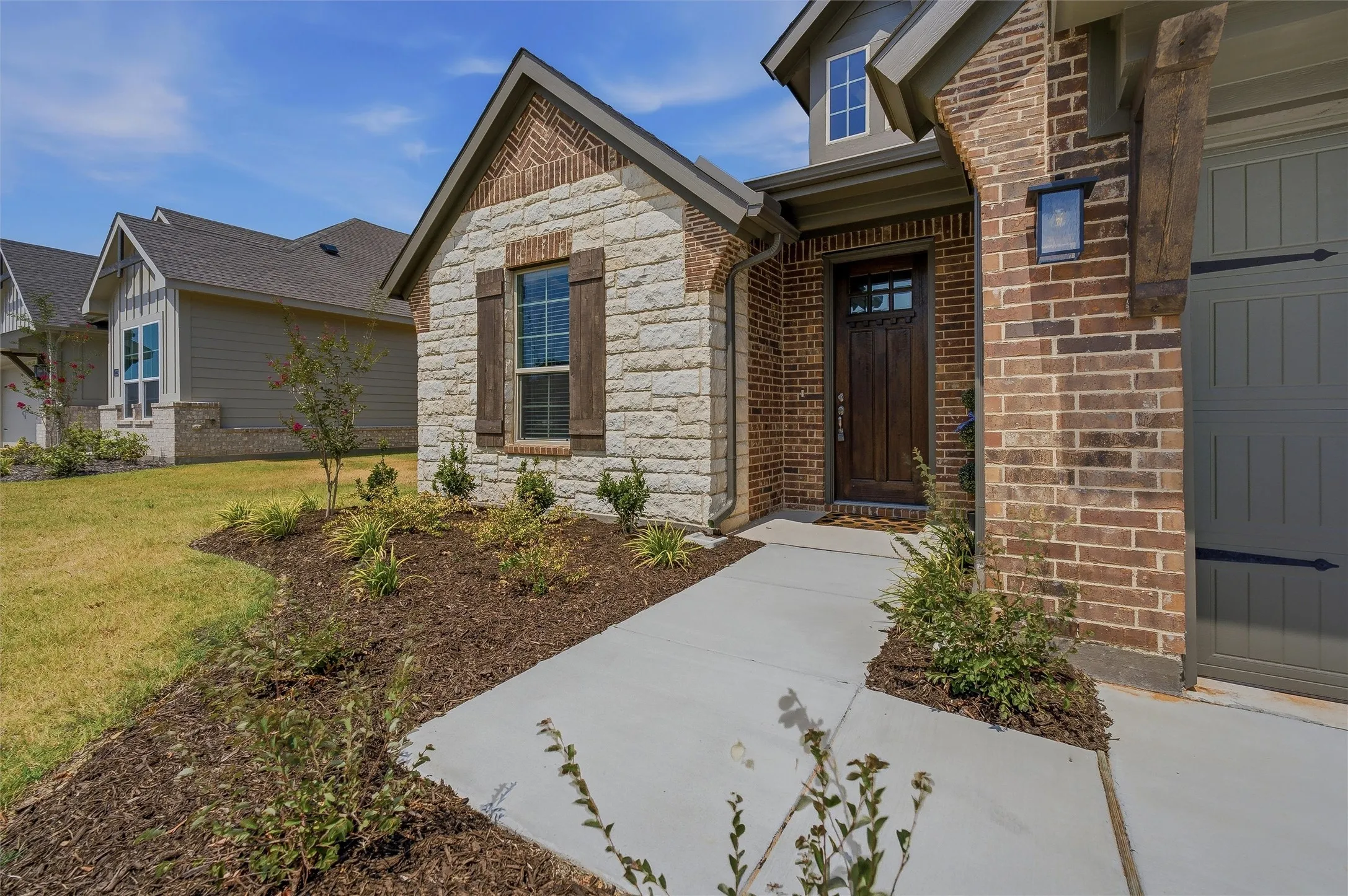 Stone and brick exterior with wood-finish shutters, a wood-paneled front door, and an attached garage