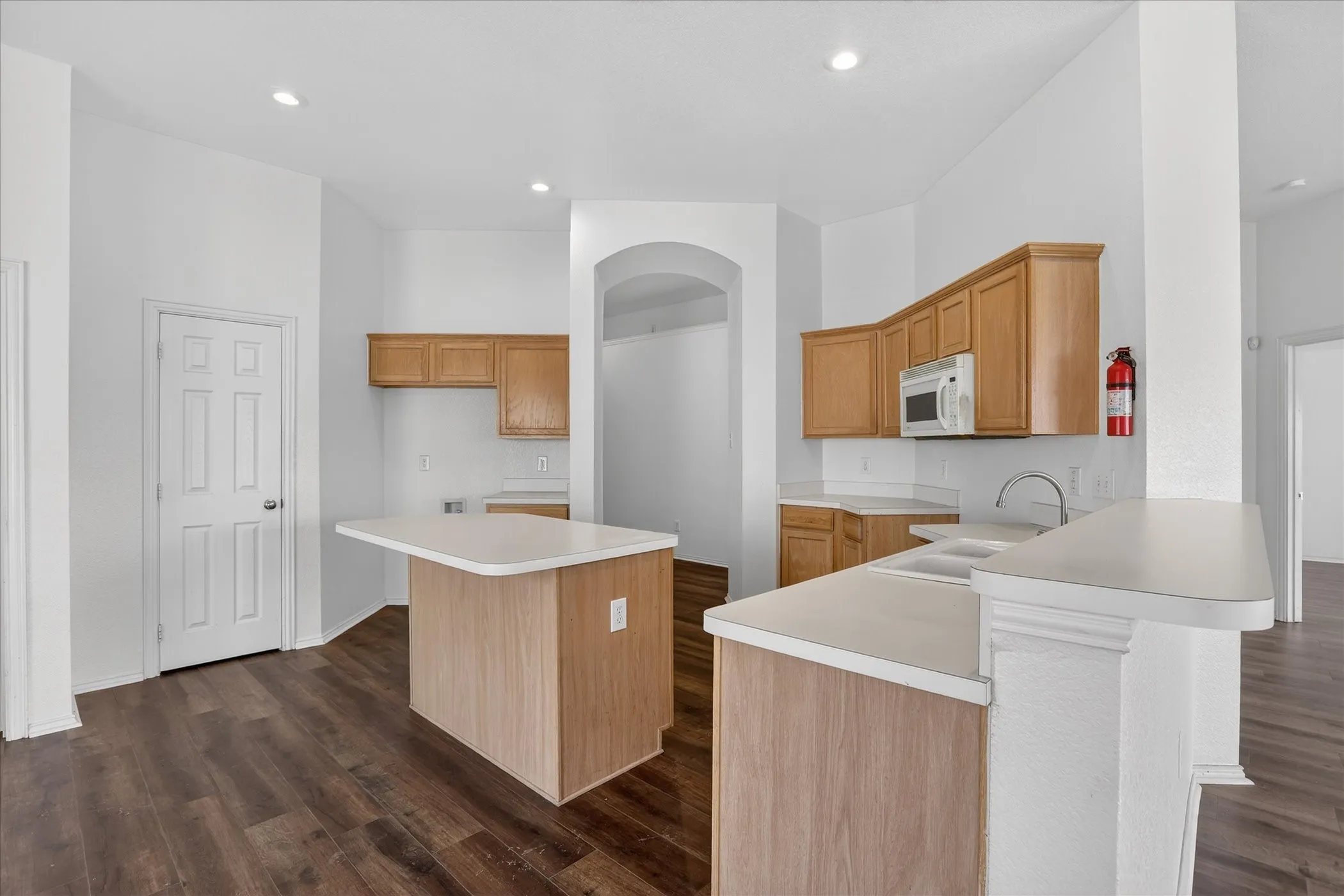 Kitchen with light countertops, a center island, a kitchen bar, dark wood-type flooring, and recessed lighting
