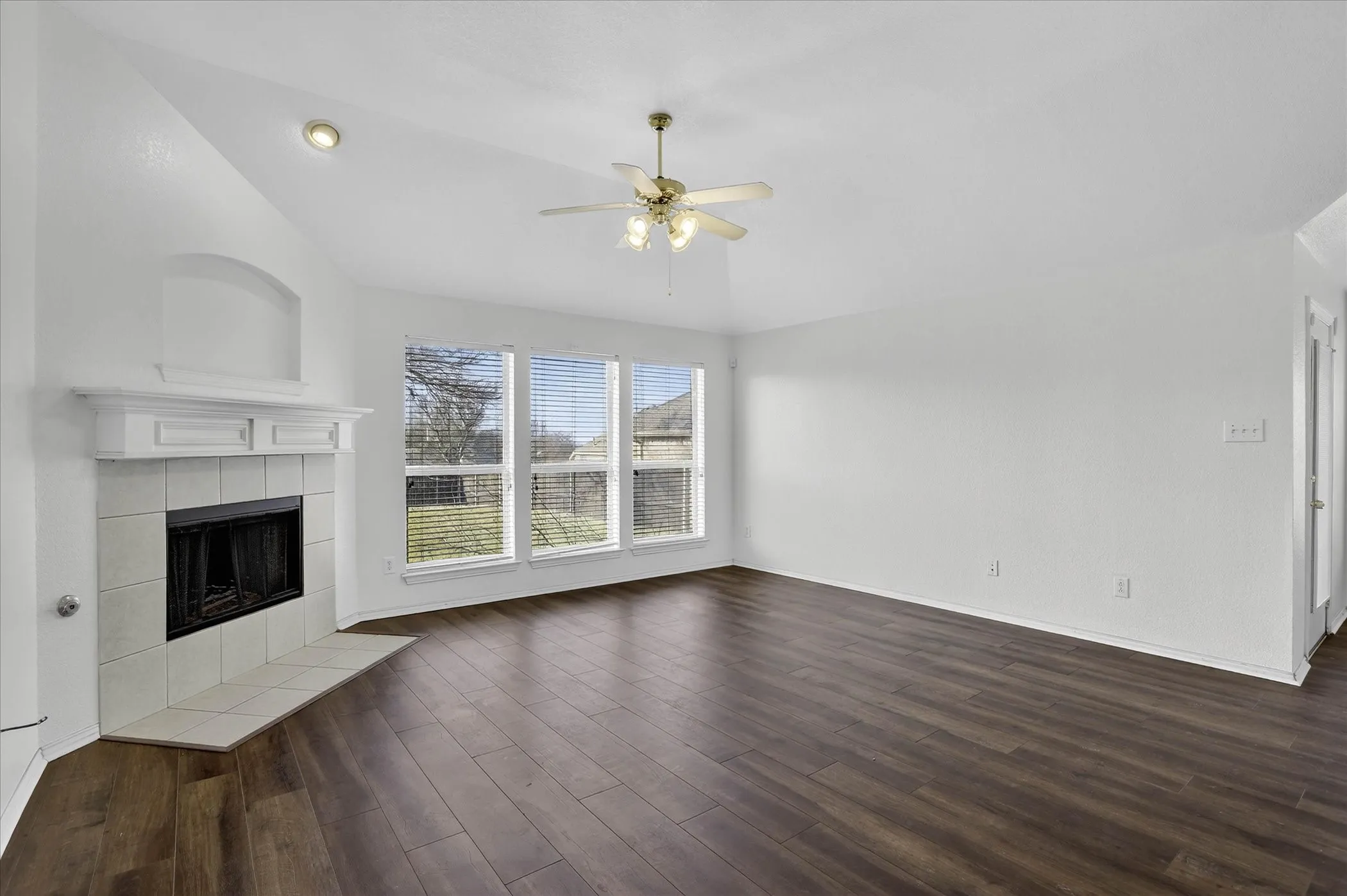 Unfurnished living room featuring vaulted ceiling, a ceiling fan, dark wood-type flooring, and a tiled fireplace