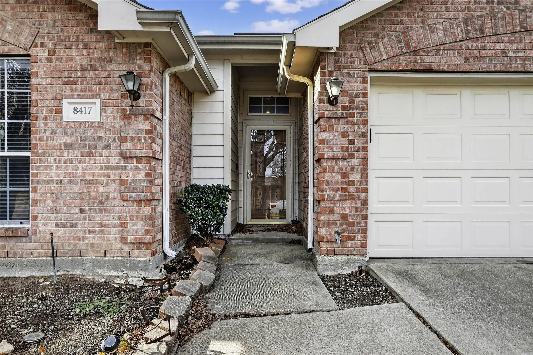 View of exterior entry with brick siding, driveway, and an attached garage
