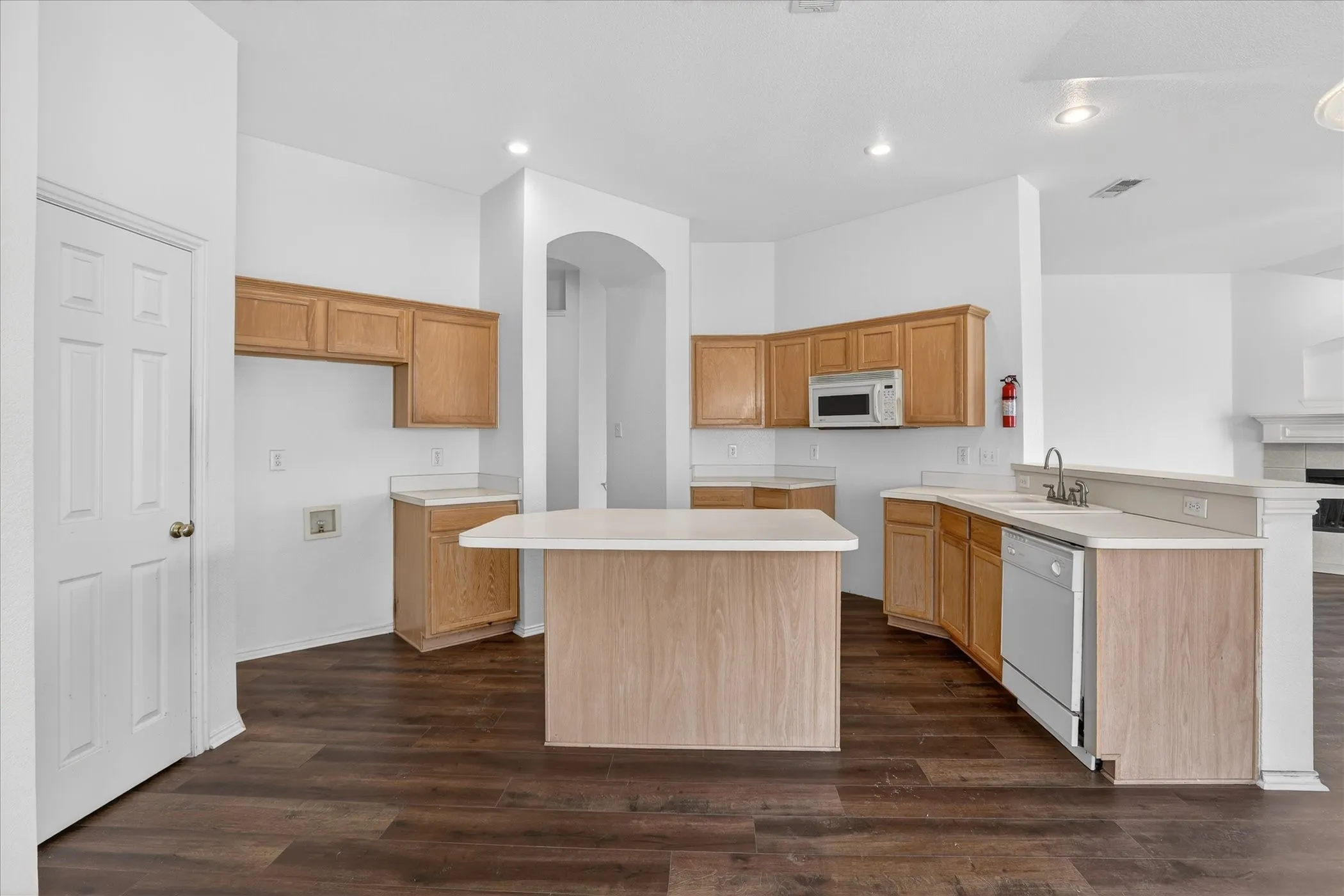 Kitchen with light countertops, a peninsula, dark wood-type flooring, white appliances, and recessed lighting