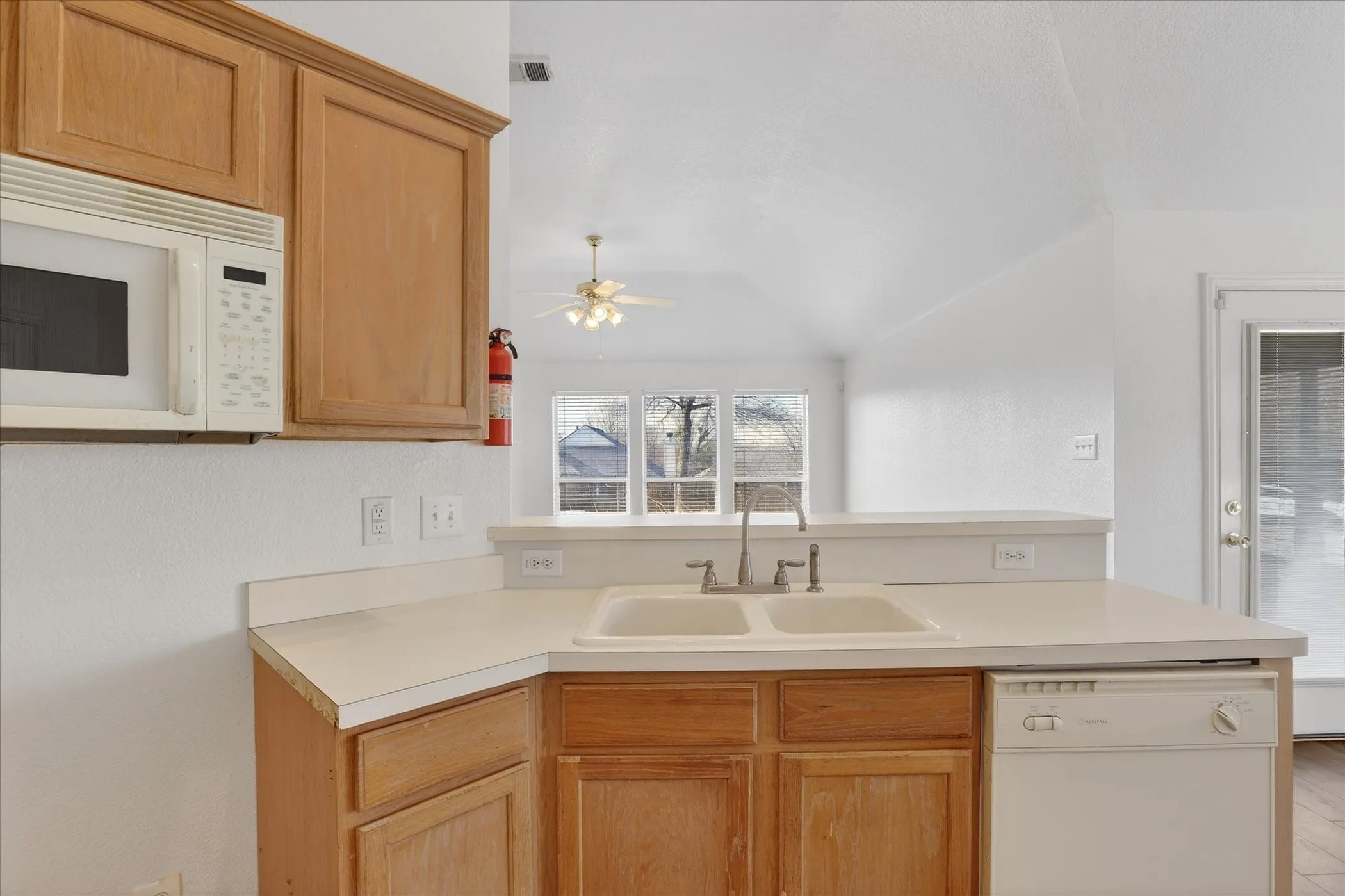 Kitchen with white appliances, light countertops, ceiling fan, a peninsula, and lofted ceiling