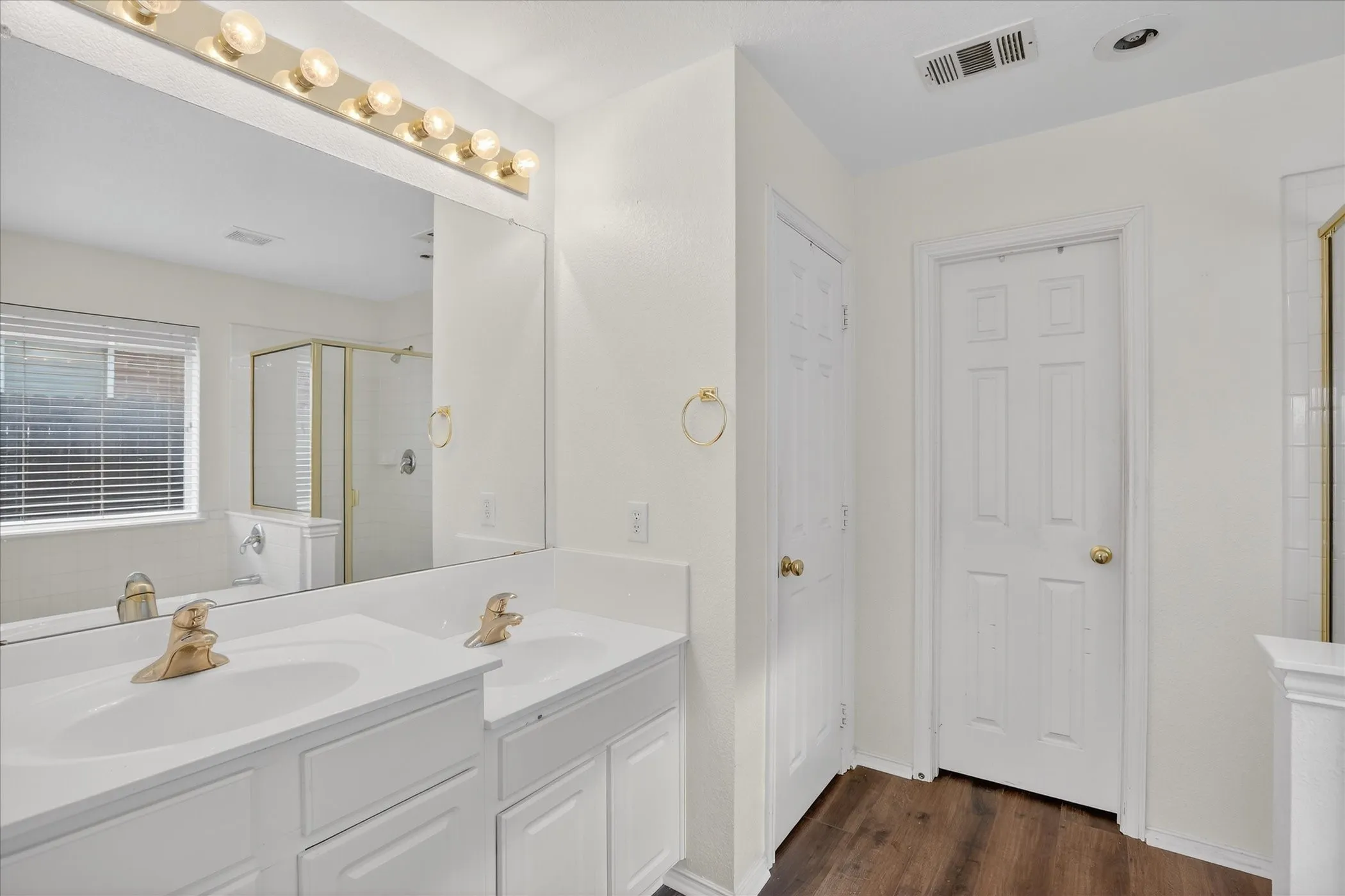 Primary B\bathroom featuring a shower stall, double vanity, and dark wood finished floors