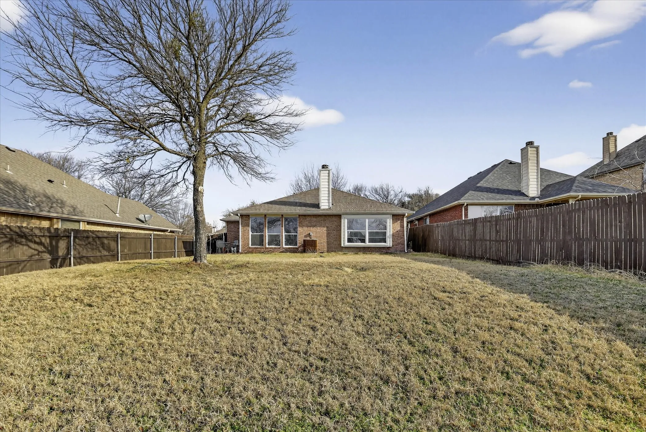 Back of house with brick siding, a fenced backyard, and a chimney