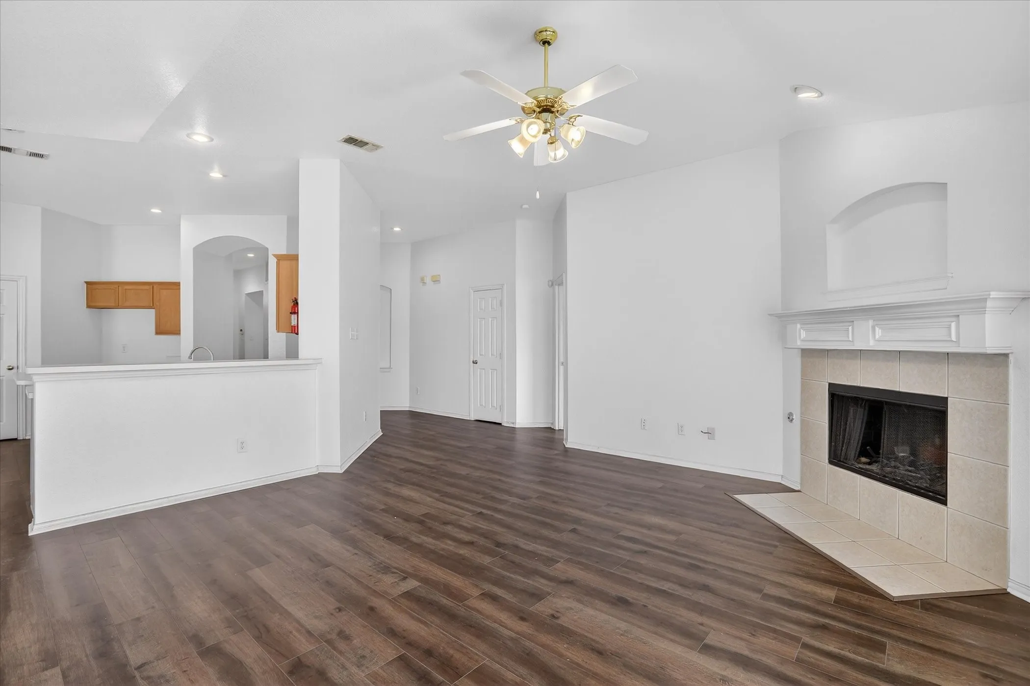 Unfurnished living room with a ceiling fan, a tiled fireplace, dark wood-style flooring, and recessed lighting