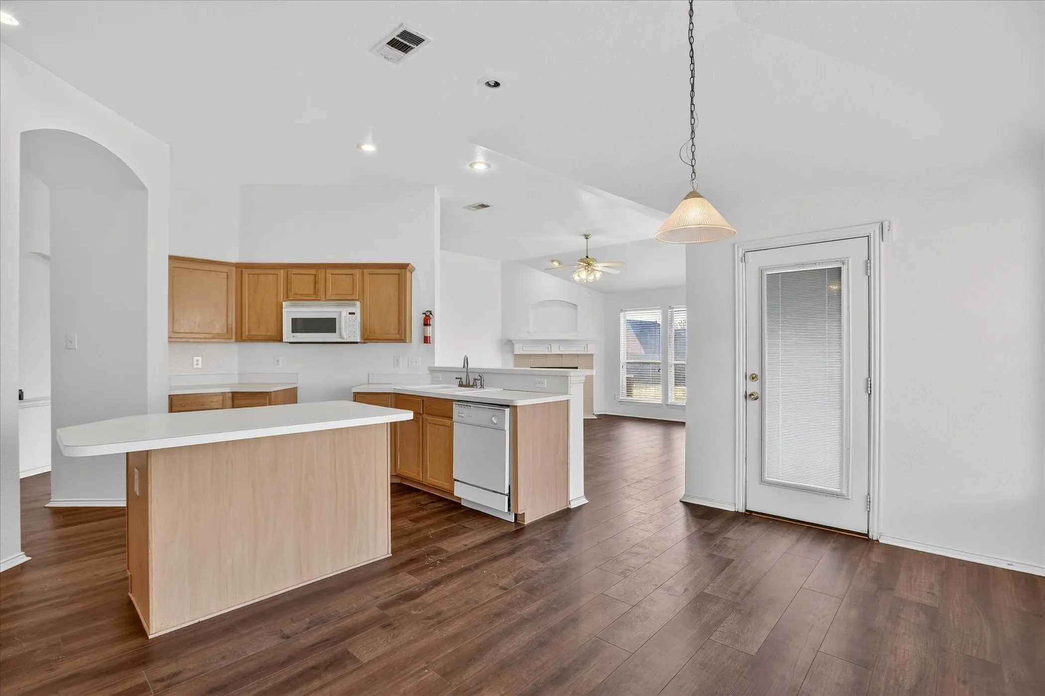 Kitchen featuring light countertops, decorative light fixtures, open floor plan, a ceiling fan, and dark wood-type flooring