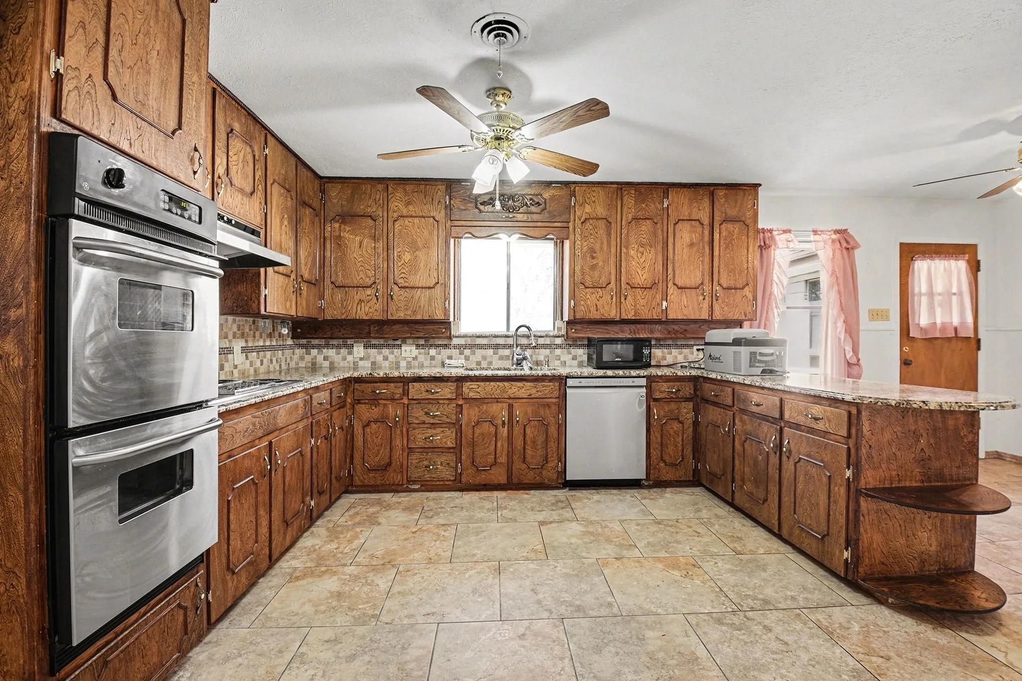 Kitchen with a ceiling fan, stainless steel appliances, a peninsula, light stone counters, and backsplash