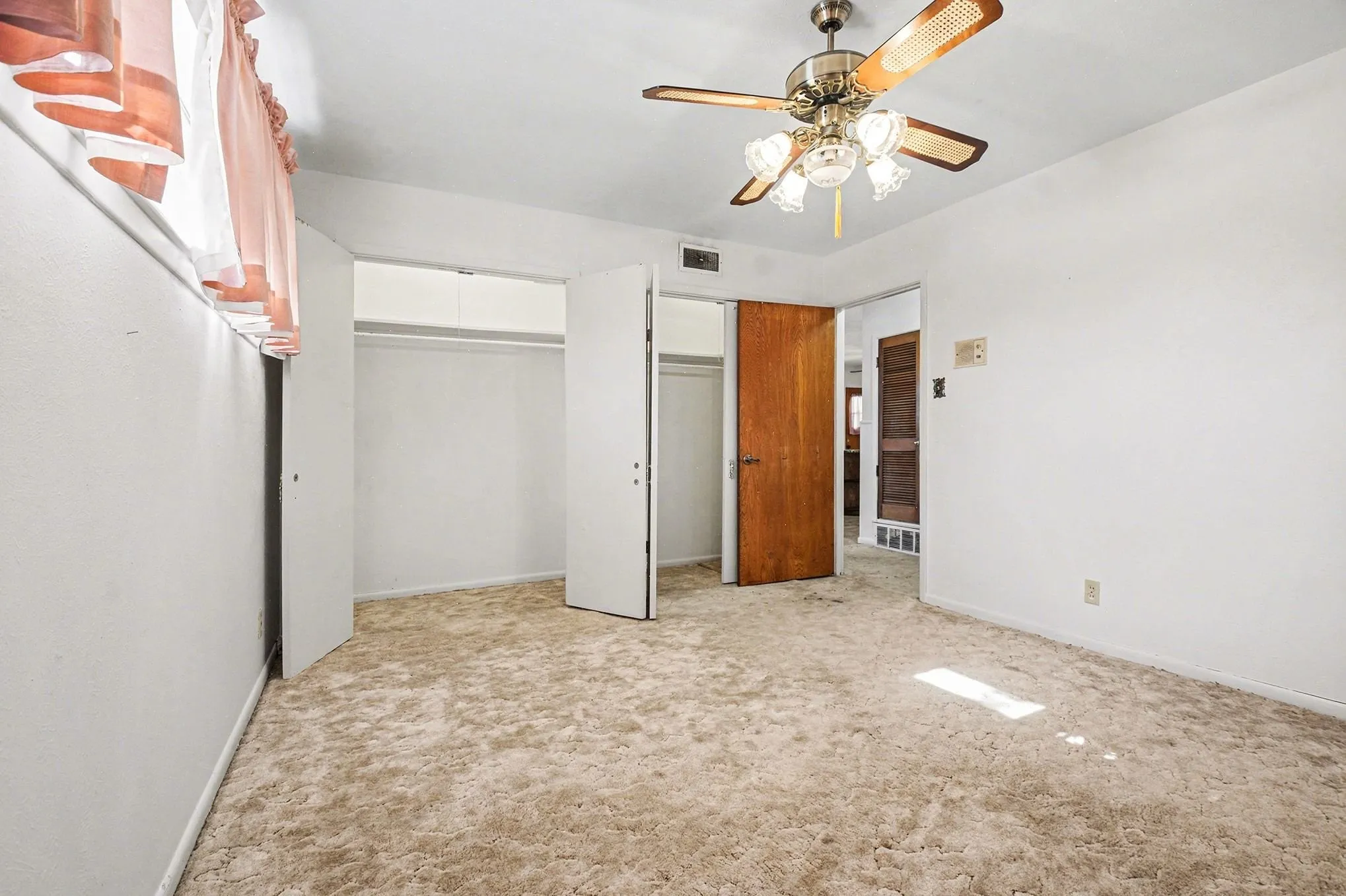 Unfurnished bedroom with light carpet, multiple closets, and a ceiling fan