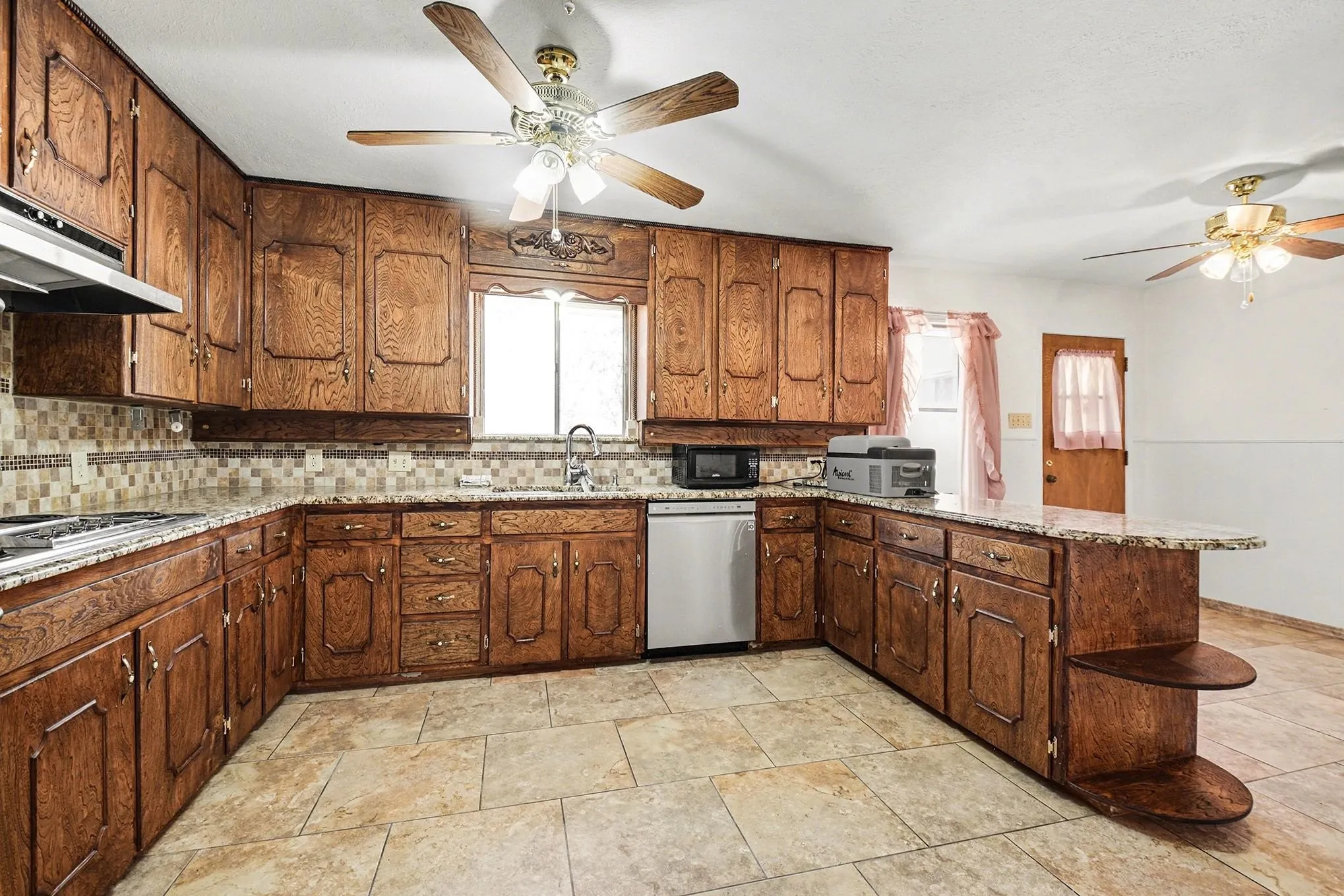 Kitchen with ceiling fan, a peninsula, light stone counters, and stainless steel appliances