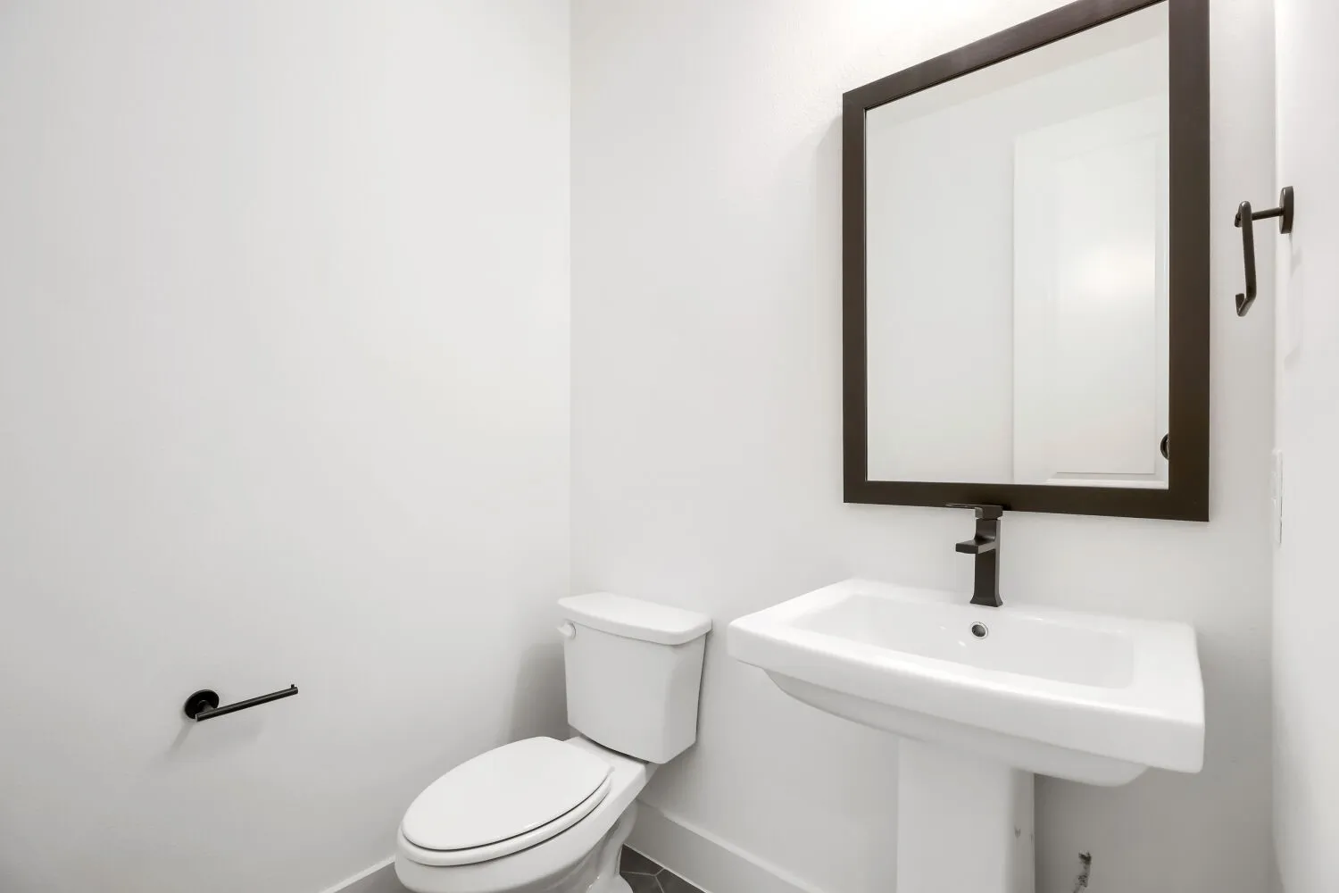 Pedestal sink with dark bronze faucet and framed mirror