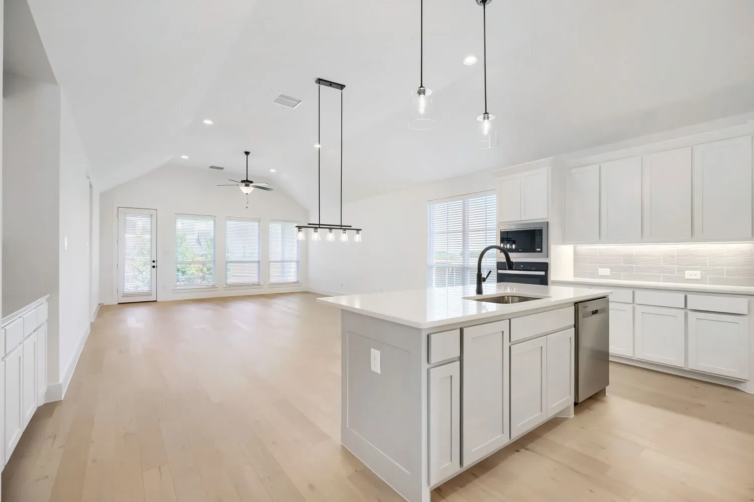 Open-concept kitchen featuring a large island with a stainless steel sink, quartz countertops, and white cabinetry